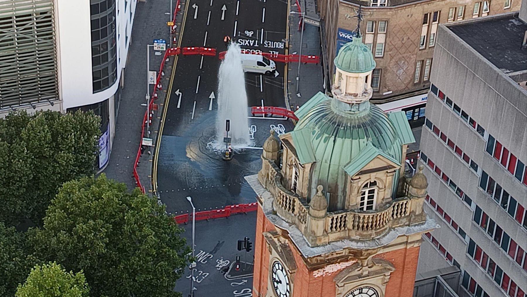 An aerial view  of a large jet of water gushing from the middle of a road