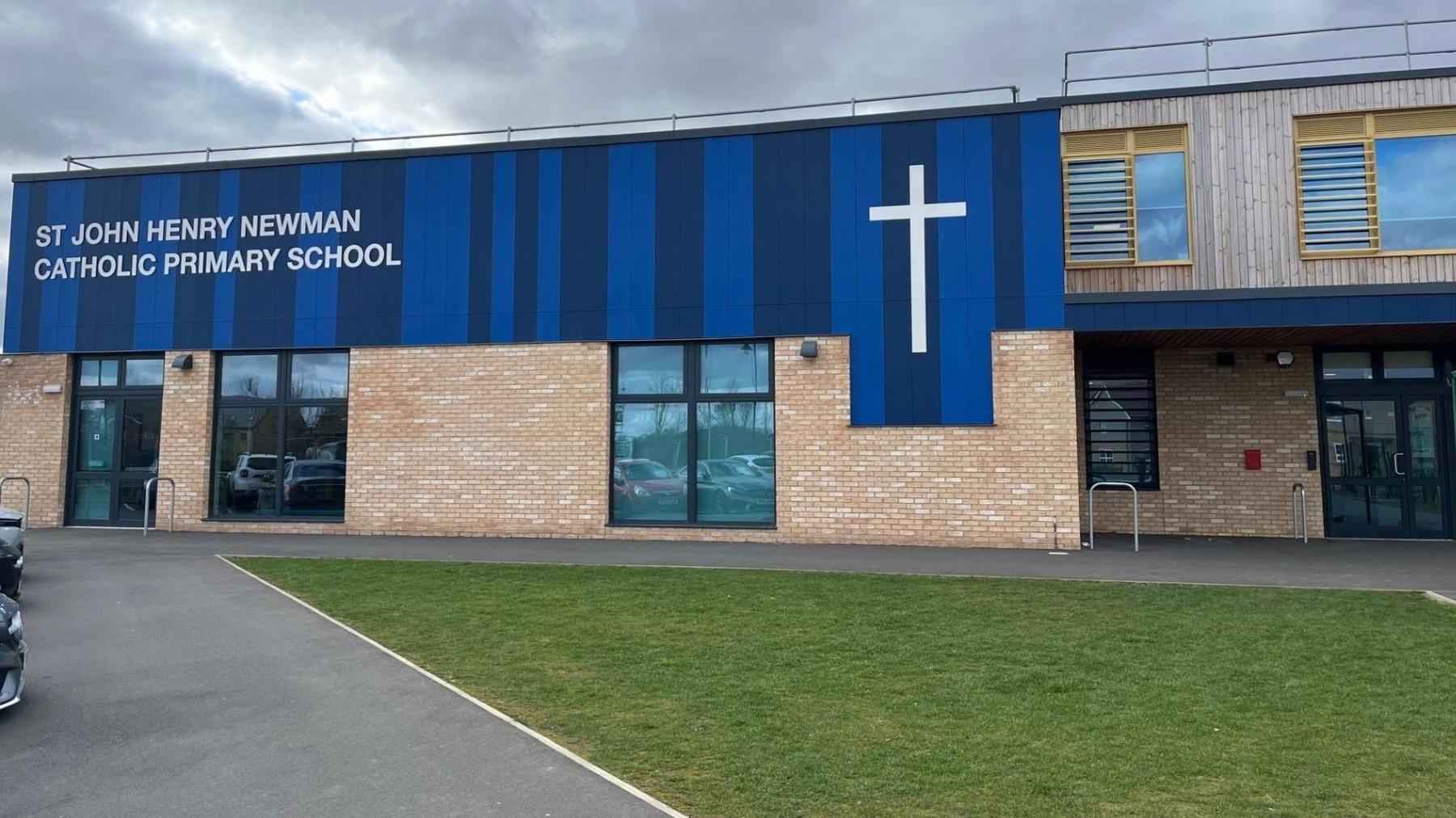 School building - with a blue name plate and a big white cross on the right side of the name plate - with grass laid in front of the building