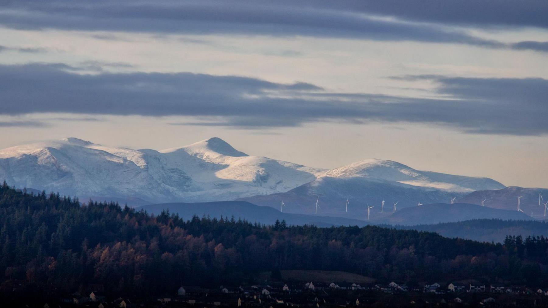View of wind turbines below snow capped mountains