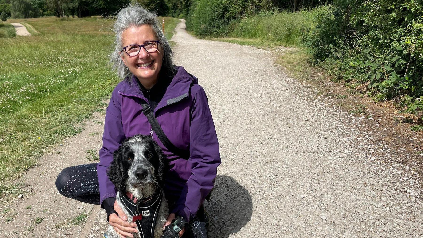 A woman crouching with her dog on a pathway
