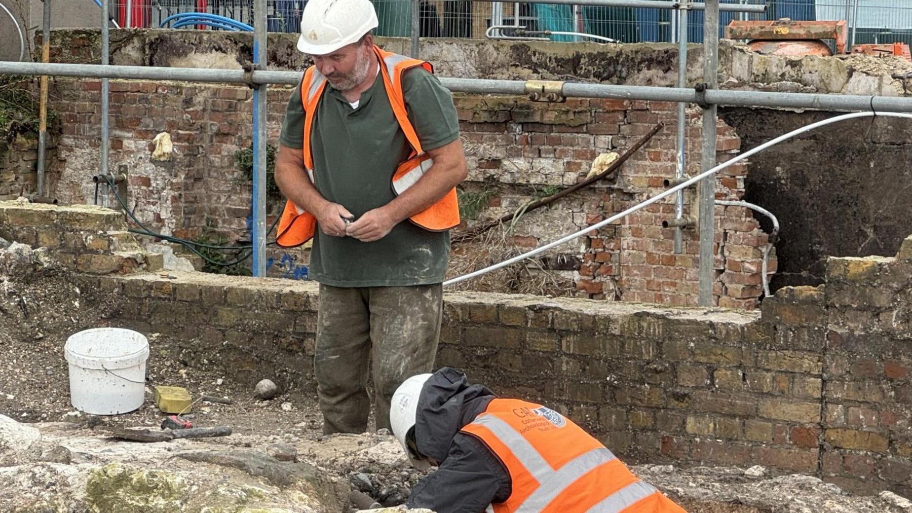 two men on site wearing hi vis, with one digging