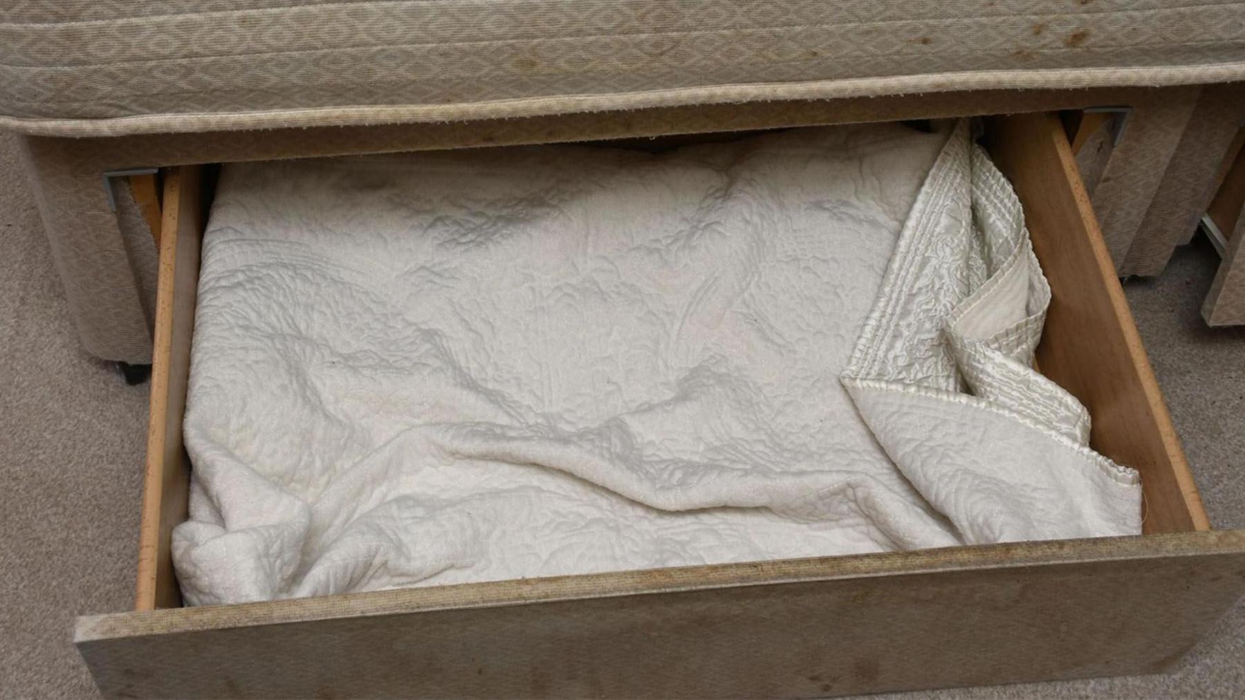 The drawer where the child was kept, open underneath a cream divan bed with a blanket inside showing where the girl lived for the first three years of her life.