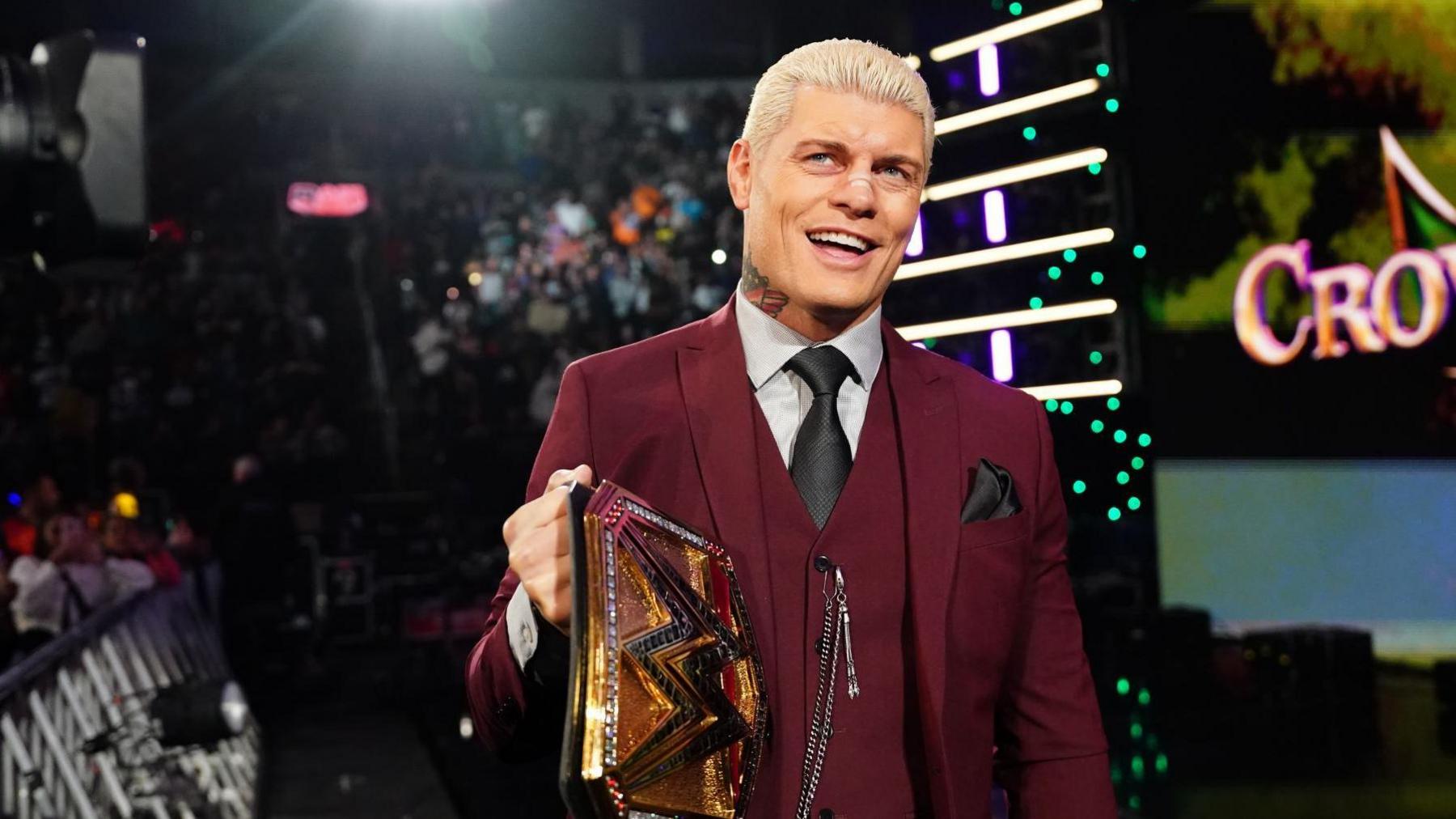 ST LOUIS, MISSOURI - OCTOBER 07: Undisputed Champion Cody Rhodes makes his entrance during Monday Night RAW at Enterprise Center on October 7, 2024 in St Louis, Missouri. He is wearing a dark red three-piece suit and carrying a gold WWE belt. He has bleached blonde hair, a black tie and pocket square and a silver chain attached to his waistcoat buttons.