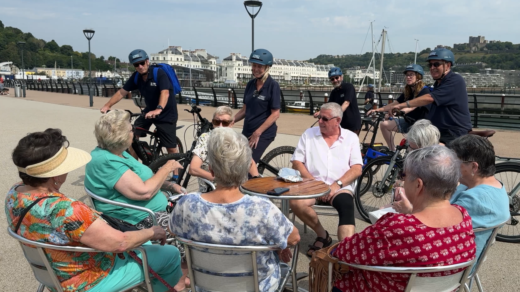 The street pastors on their bicycles talk to a group of elderly people drinking coffee