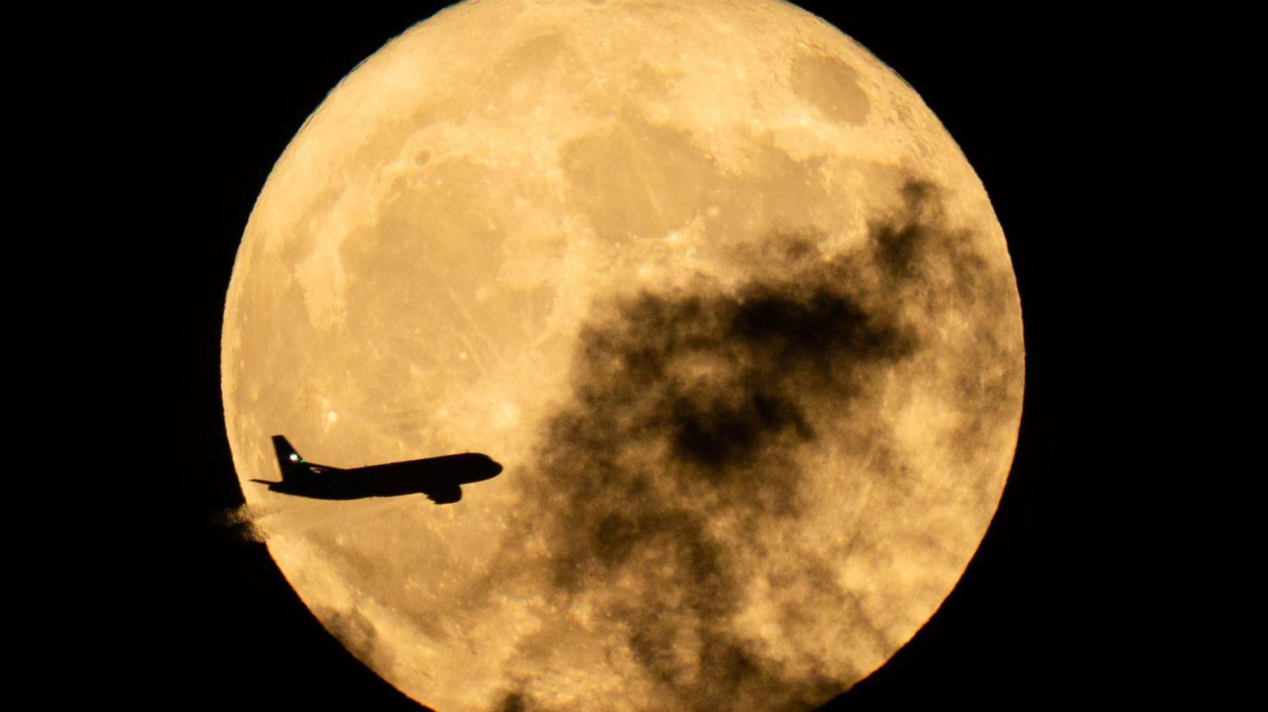 A plane flies in front of the full Moon