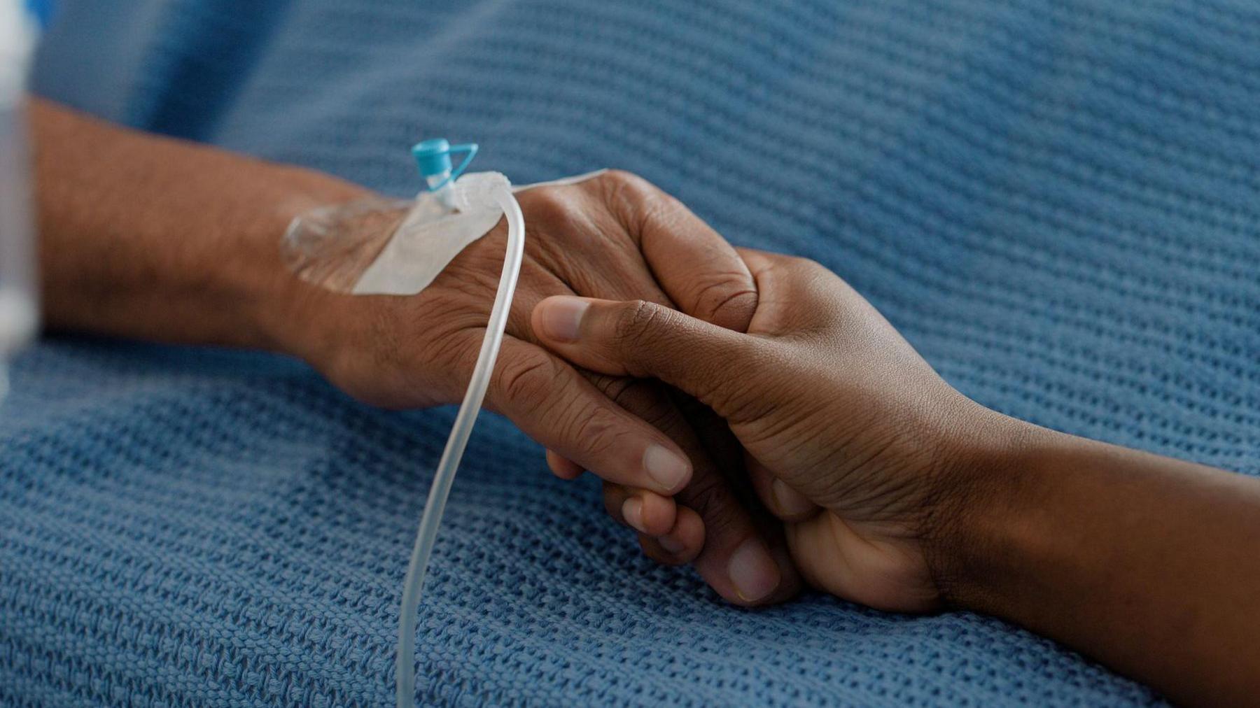 Two people hold hands across a hospital bed. 