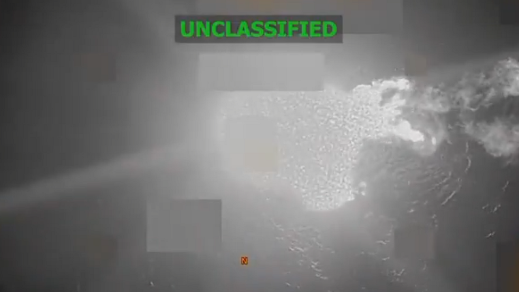 What appears to be a black and white image of the sea as seen from above. A few areas are blurred, including the section where the boat is. A large white area which appears to be the flames of an explosion are in the centre of the image. The word "unclassified" is captioned on the image.