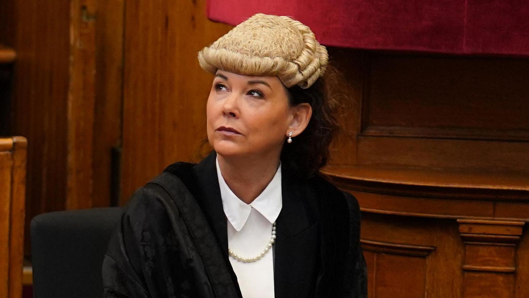 A woman wearing a wig and gown sits in a court