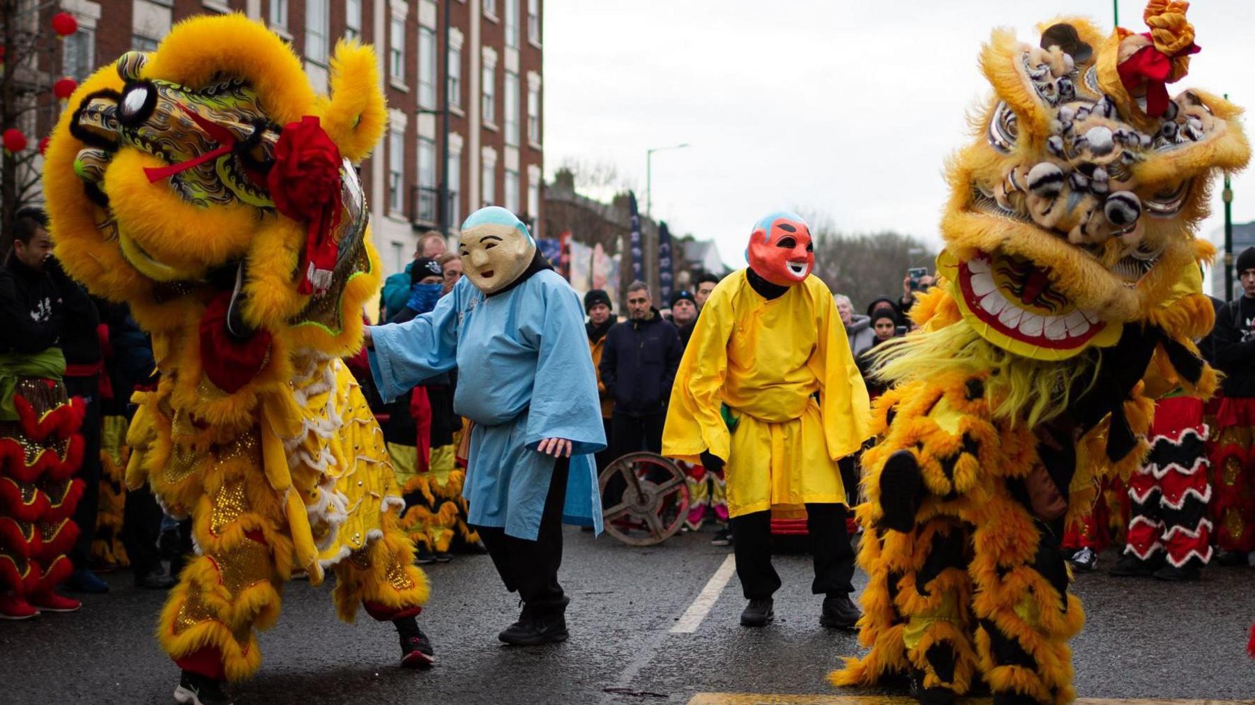 Two yellow lions perform in Liverpool's Chinatown surrounded by a group of people