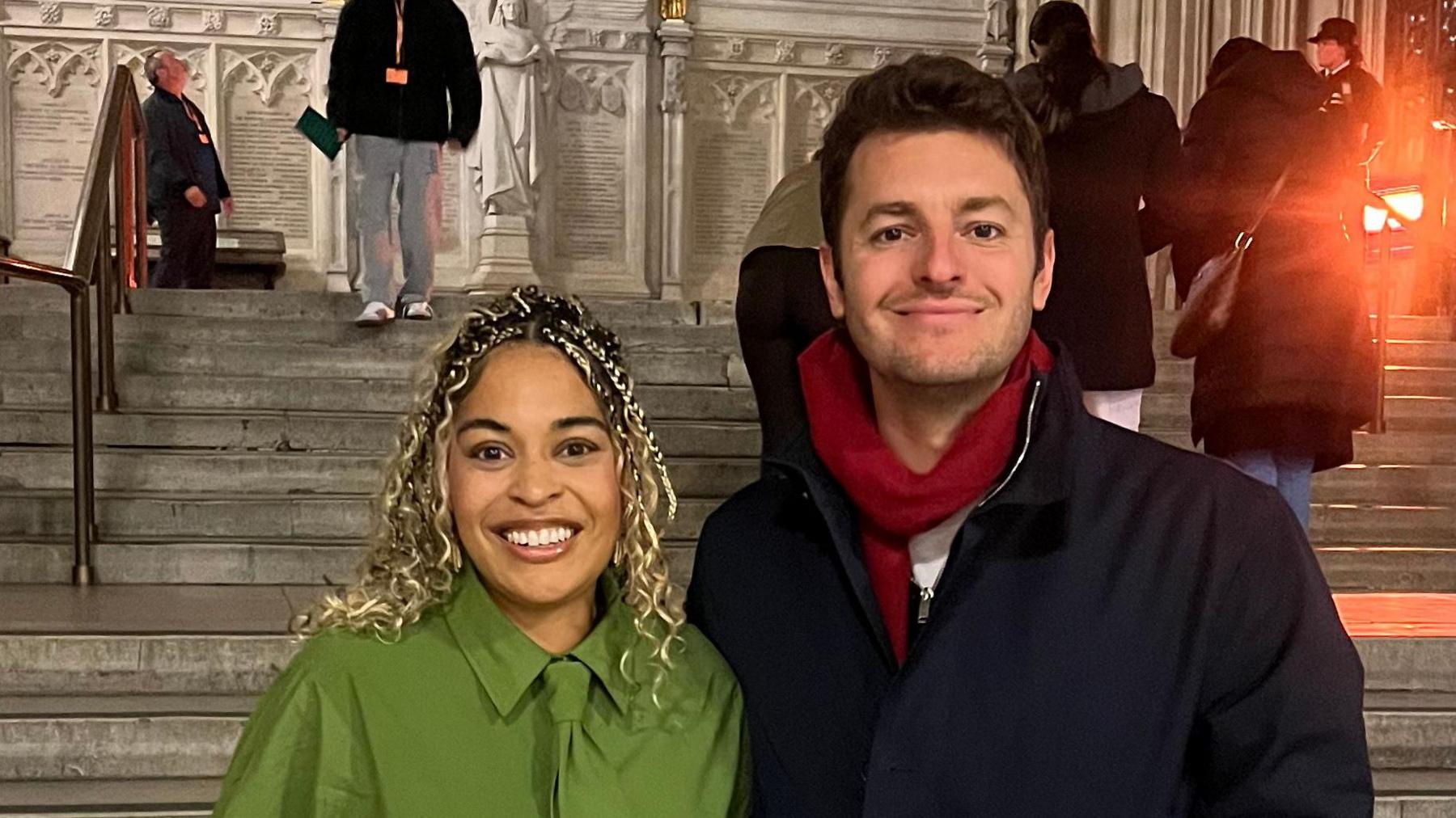 Mrs Soanes stands at the bottom of some steps alongside MP Jack Abbott. She wears a green shirt with a matching green coloured tie. Abbott has dark hair and wears a black coat with a red scarf.