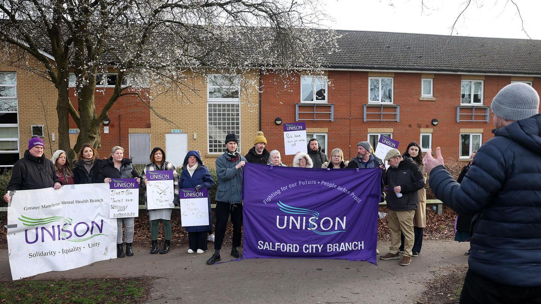 Protestors hold up UNISON purple and white sign in a demonstration outside the care home