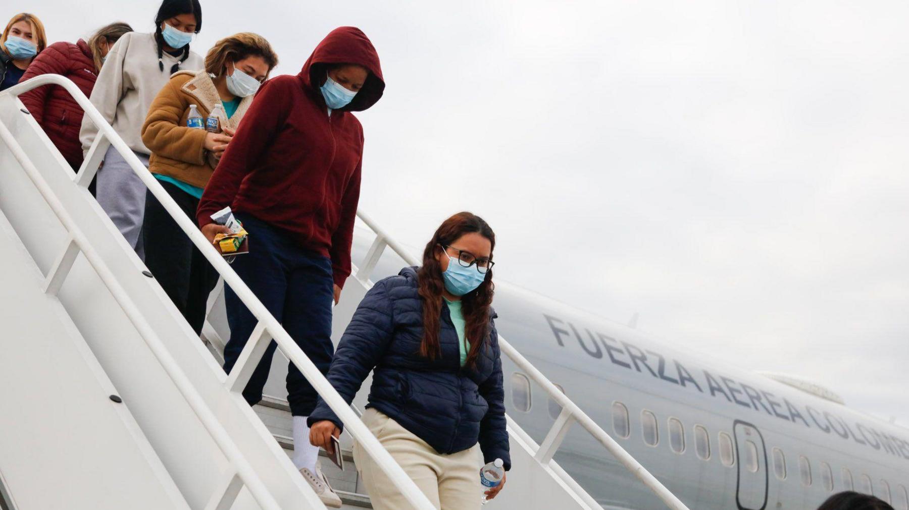 Five women wearing face masks and holding their passports in their hands disembark from a Colombian Air Force plane in Bogota