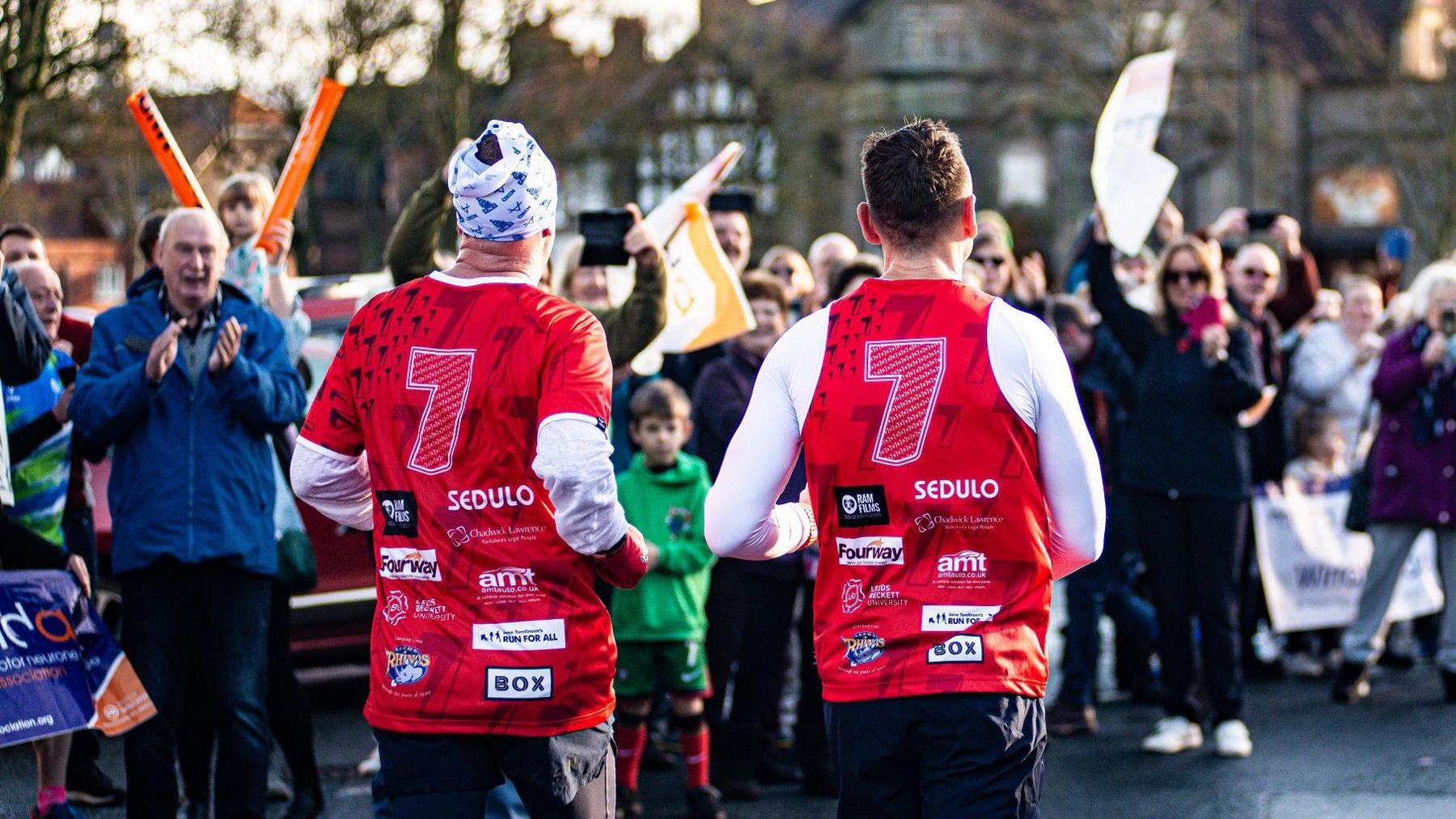 View of the number 7 on the backs of Sinfield and his running teammate as they run through a crowd of well-wishers cheering and applauding on a residential street