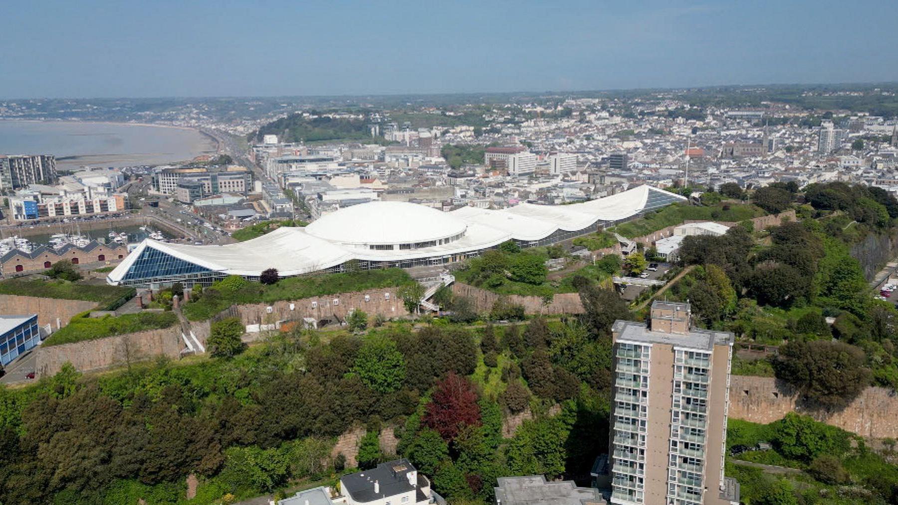 An aerial view of Fort Regent, a large white building on top of a hill, looking west.