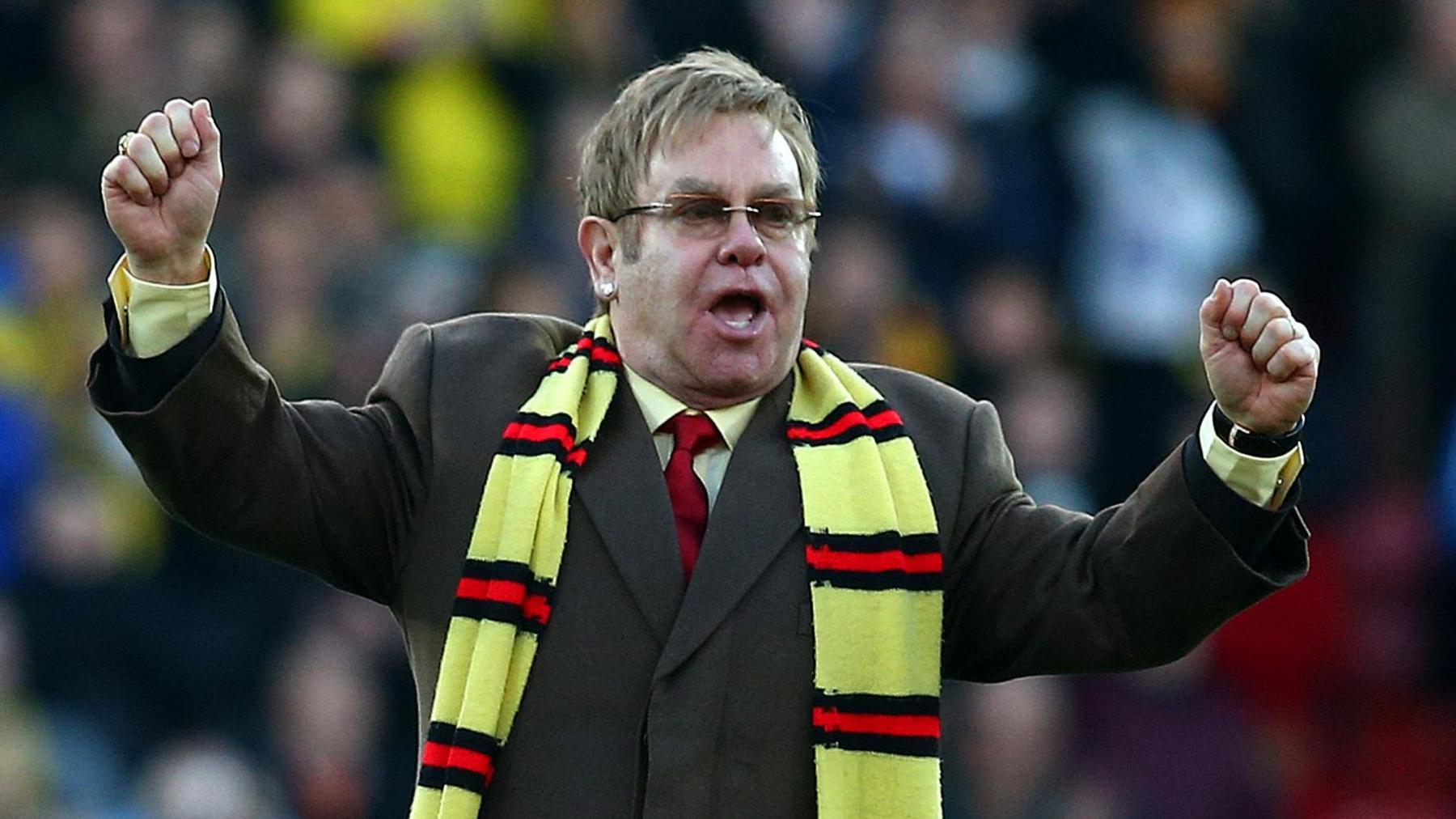 Elton John stood on the pitch at Vicarage Road wearing a scarf and cheering