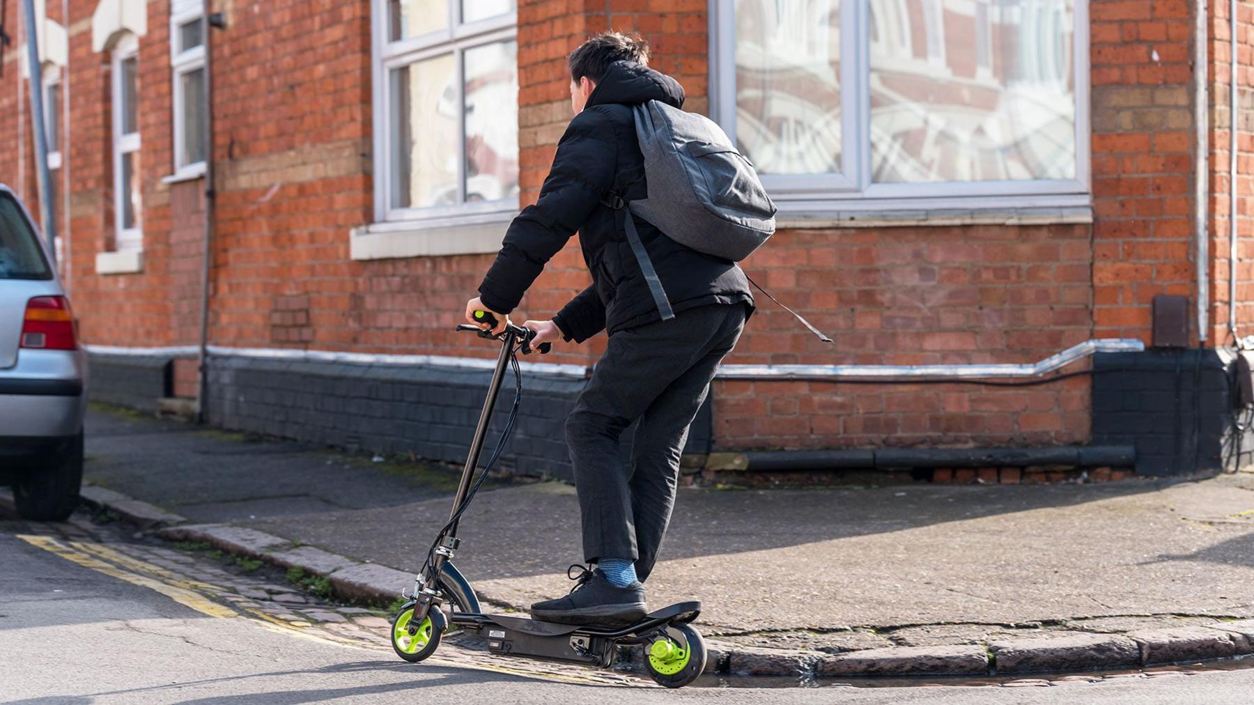 A boy riding an e-scooter on a residential street in the united Kingdom