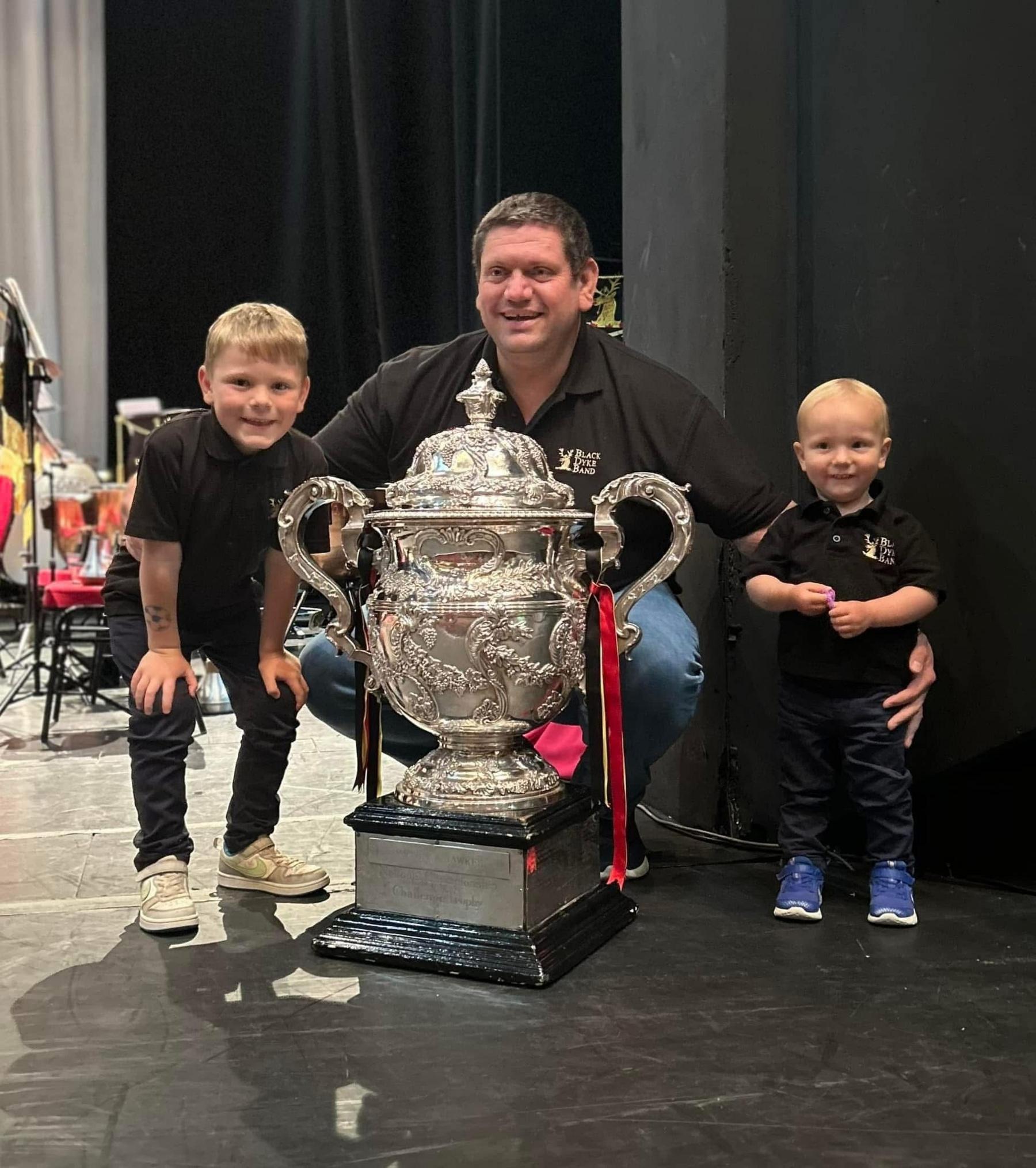 Gavin Saynor o flaen cwpan arian enfawr gyda dau o'i feibion