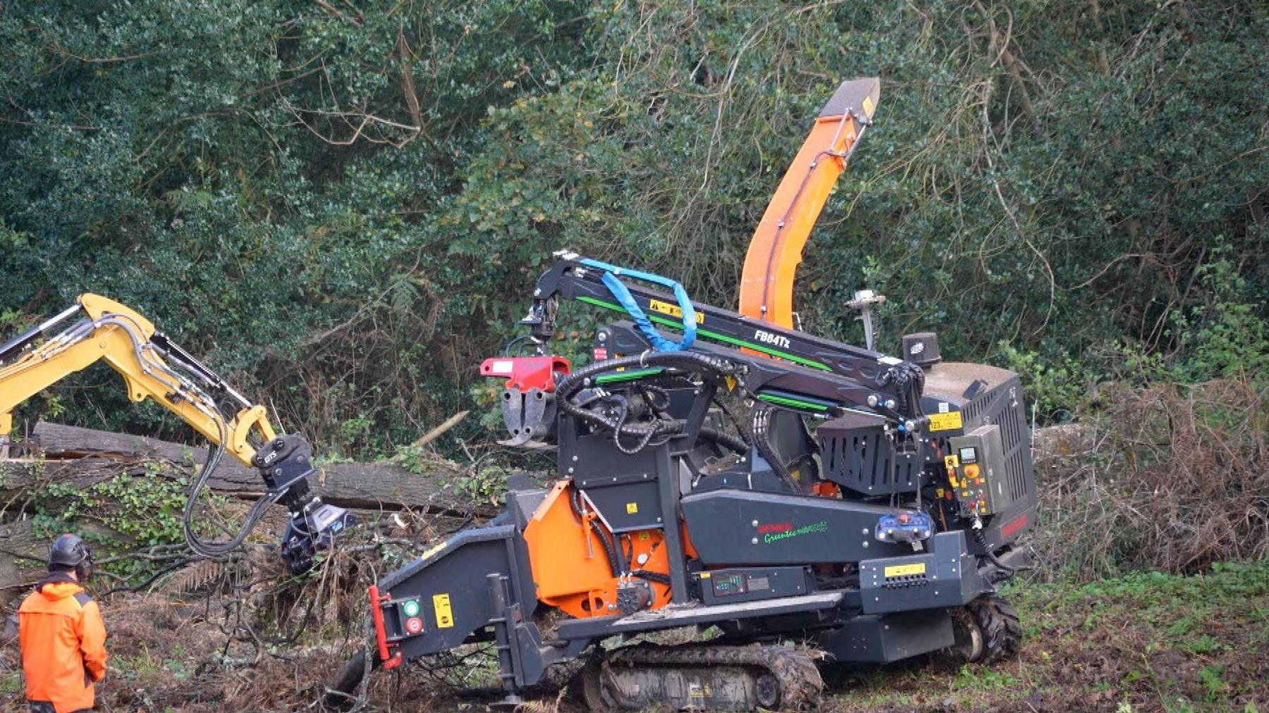 Workers in hi-vis jackets use a chipper to clear tree debris