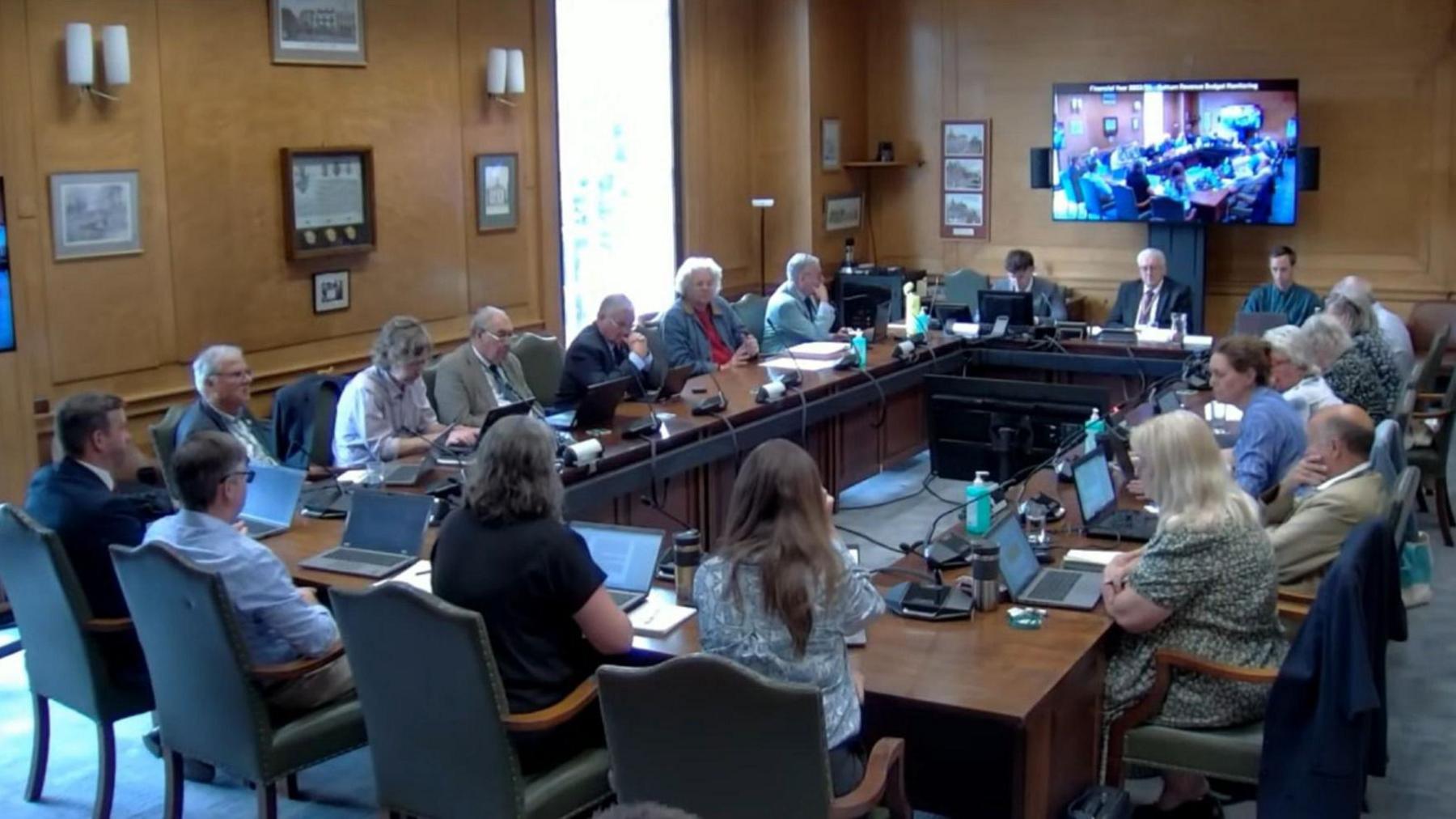 Male and female councillors sitting around a table with laptops placed on their desks in front of them