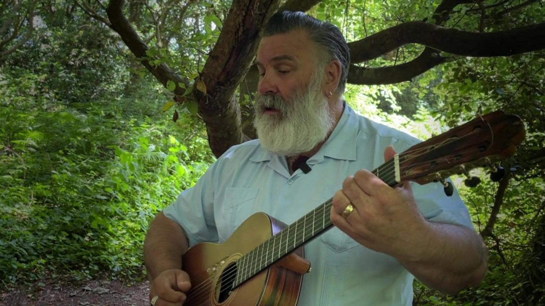 Paul Armfield playing guitar in a woodland surronded by trees