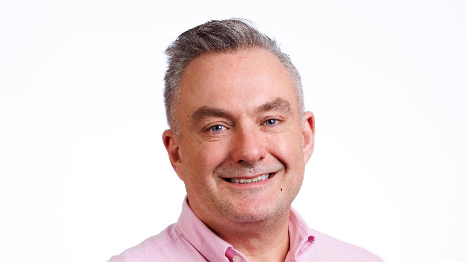 A head shot of Paul Bytheway, wearing a pink shirt with a white background