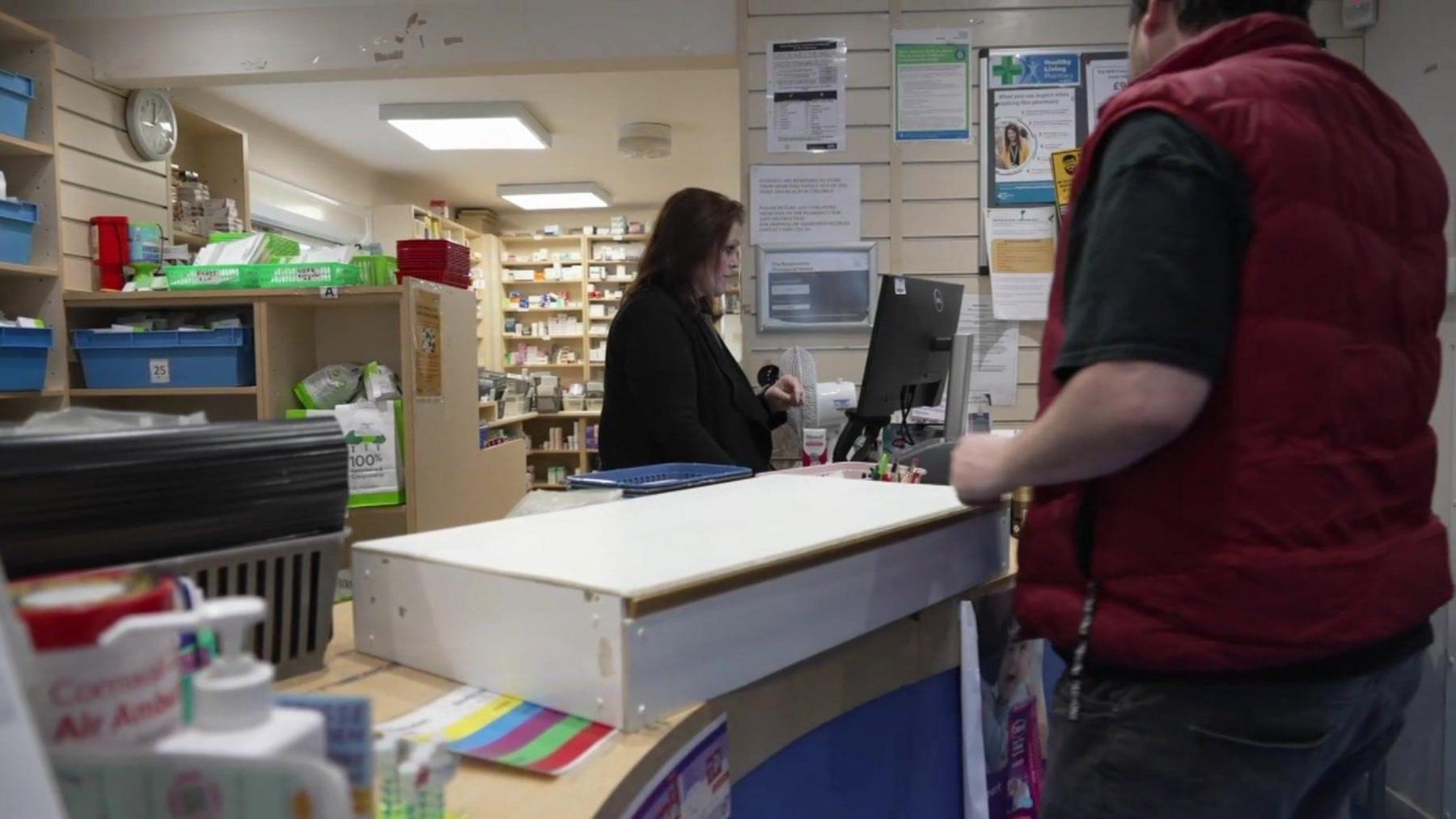 A woman serving a man in a pharmacy.