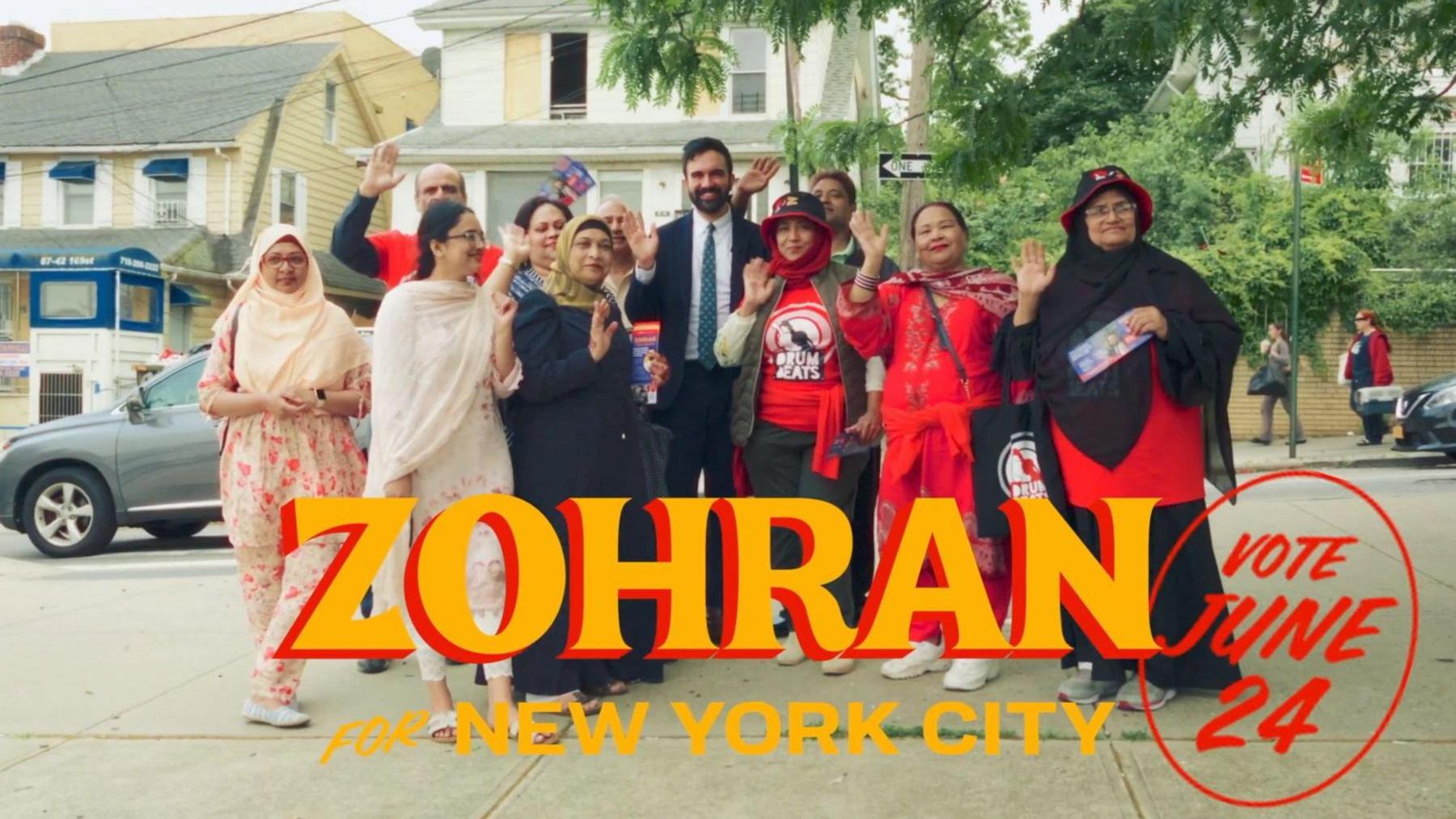 New York Mayor Zohran Mamdani standing between a group of men and women. Women are wearing traditional south asian clothes. 