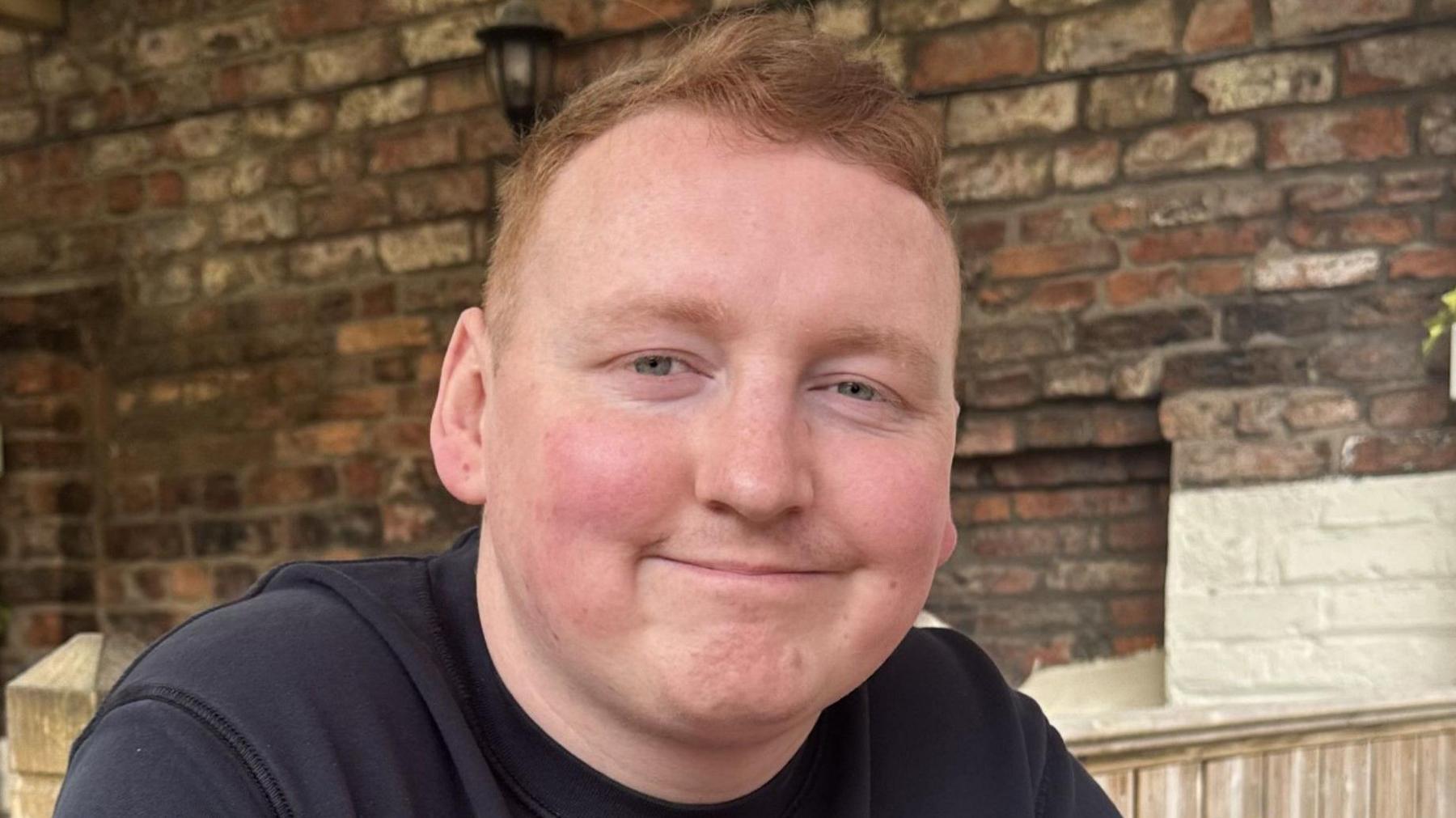 A man with red hair smiles at the camera