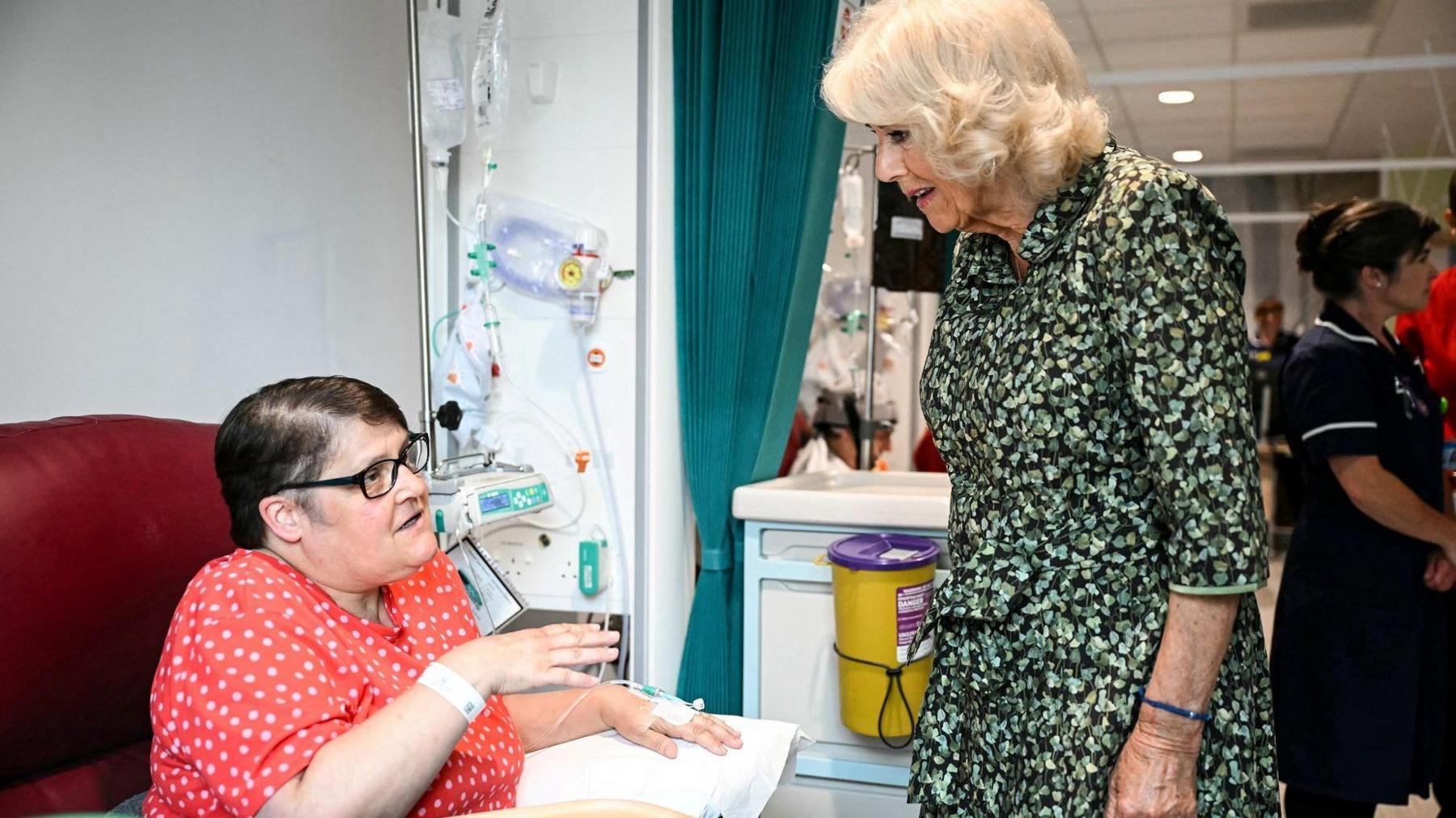 The Queen stands next to a cancer patient who is sitting while getting treatment