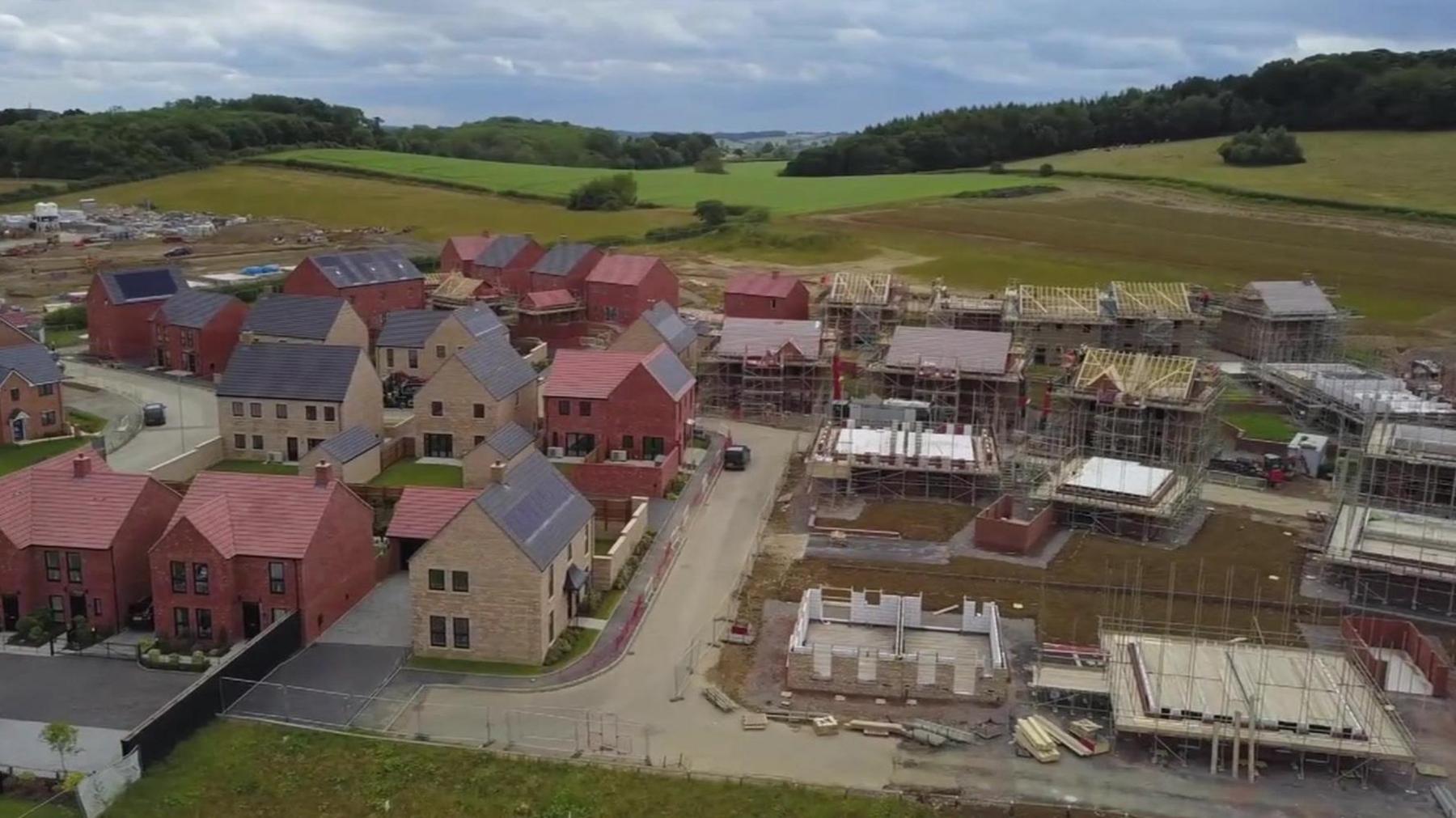 Drone view of a building site of houses being built with green fields in the background