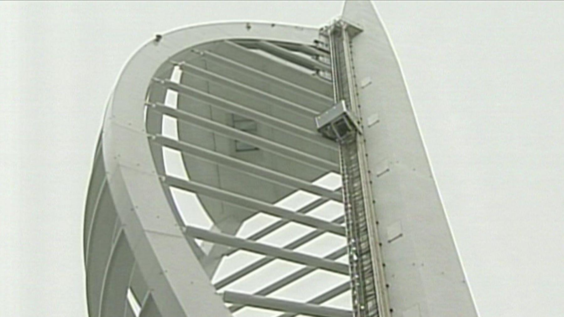 A lift on the outside of the Spinnaker Tower, a white architectural structure with a curved design and horizontal beams forming an open, skeletal framework.