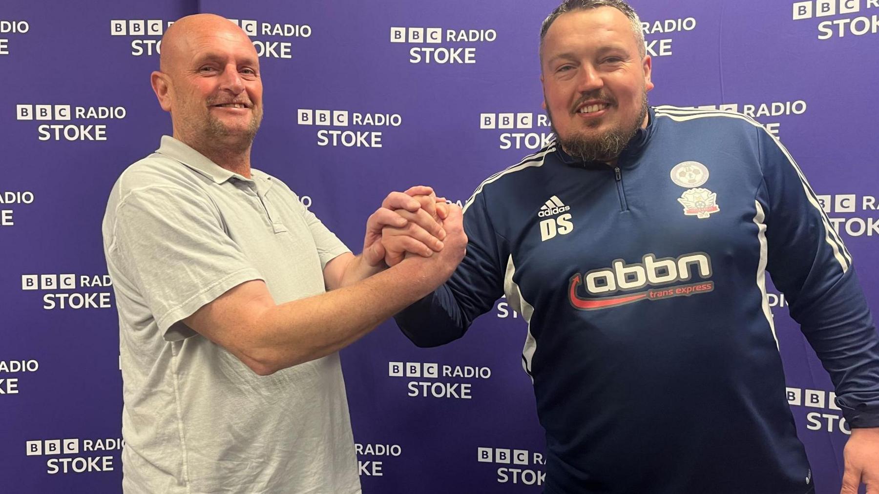 A man with a white t-shirt shaking hands with a man in a blue football top. Both are looking at the camera and behind them is BBC Radio Stoke signs on a purple background. 