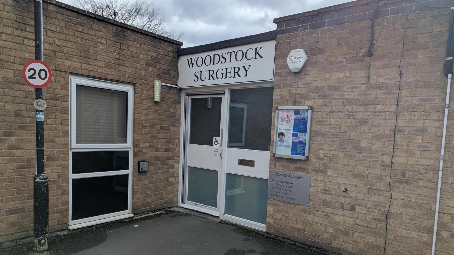The front of Woodstock Surgery - which is a small flat roofed building on the bend of a road.