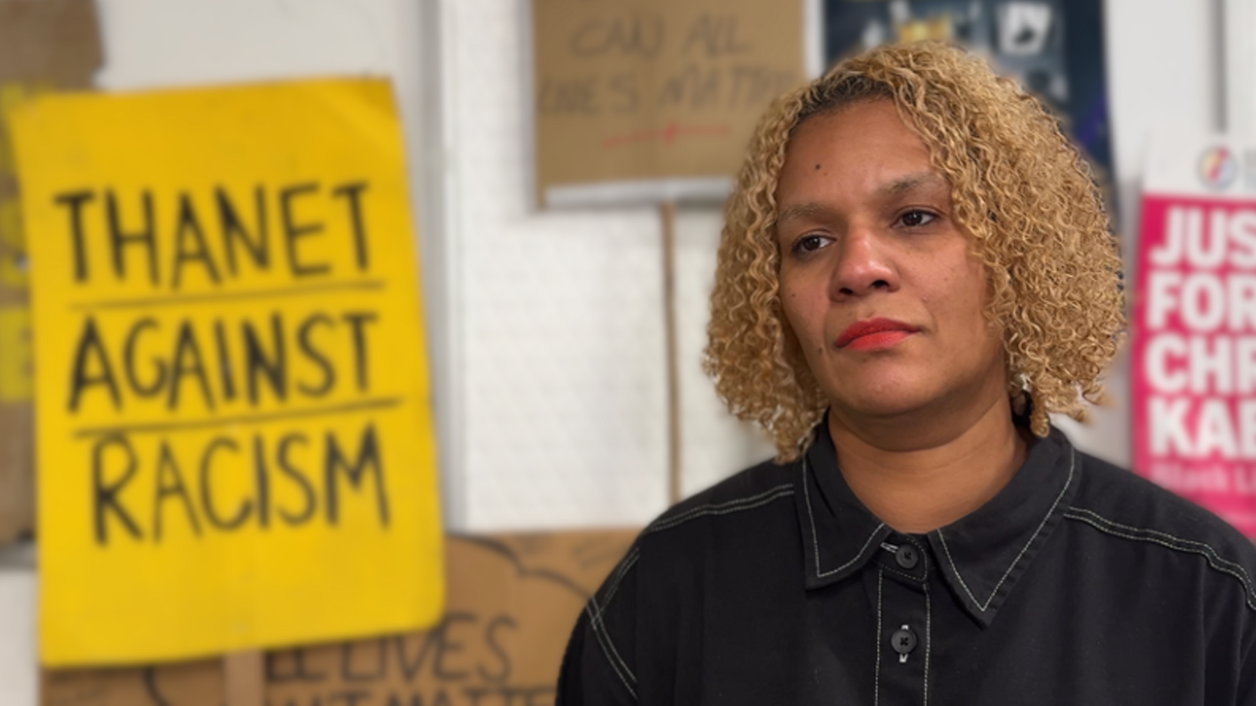 A woman stands in front of placards which reads Thanet against racism