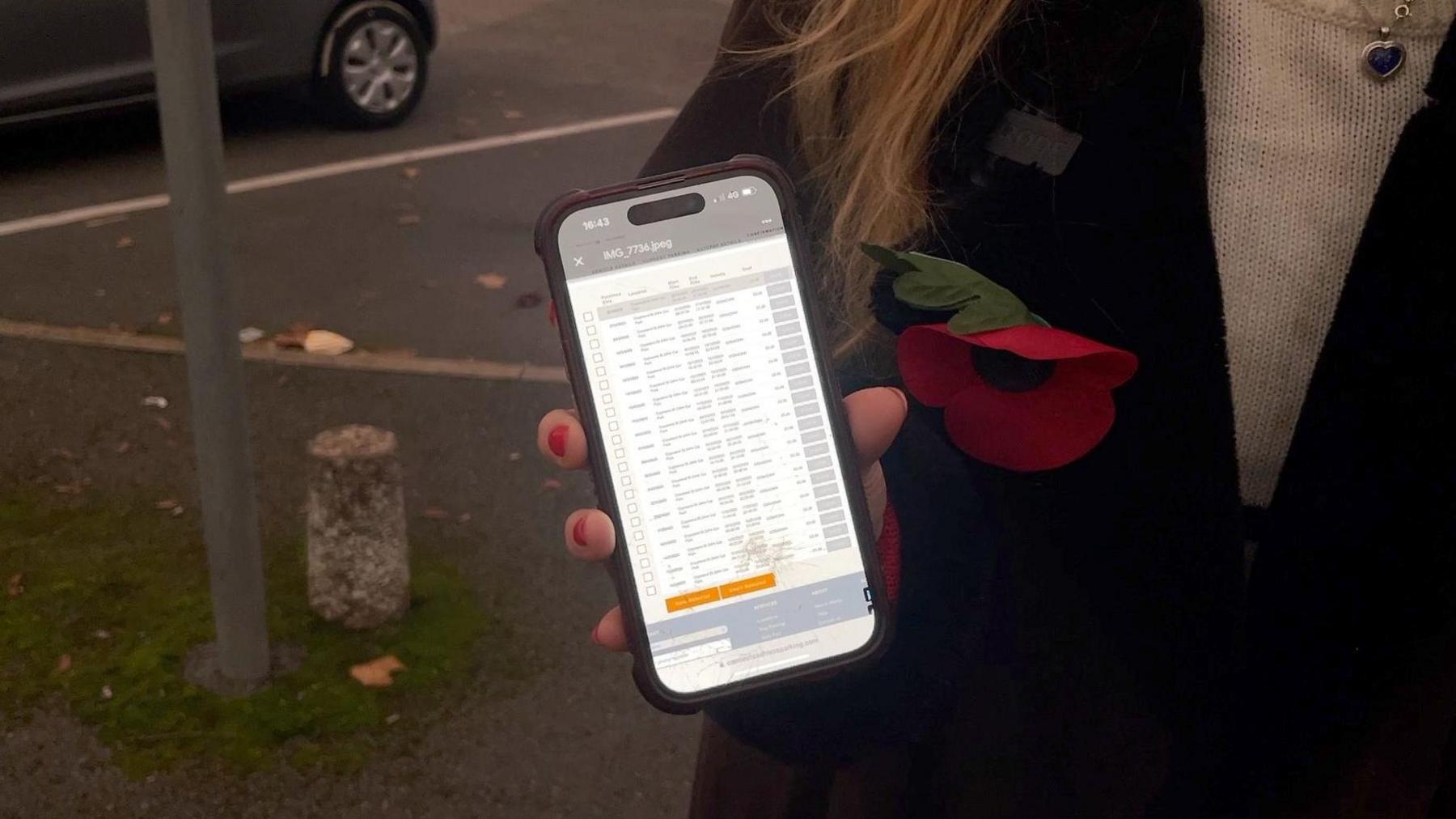 Miss Hudson holding up her phone, showing her parking receipts