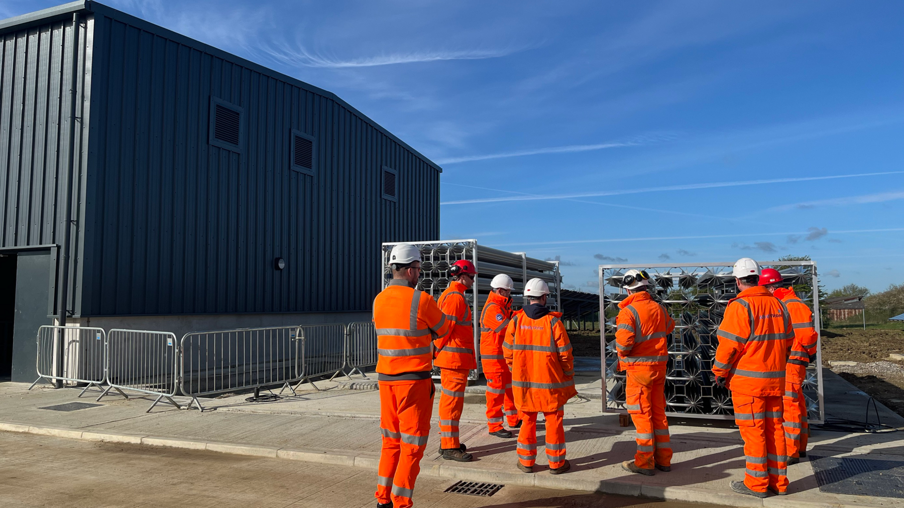 Grey building with workmen outside in orange gear