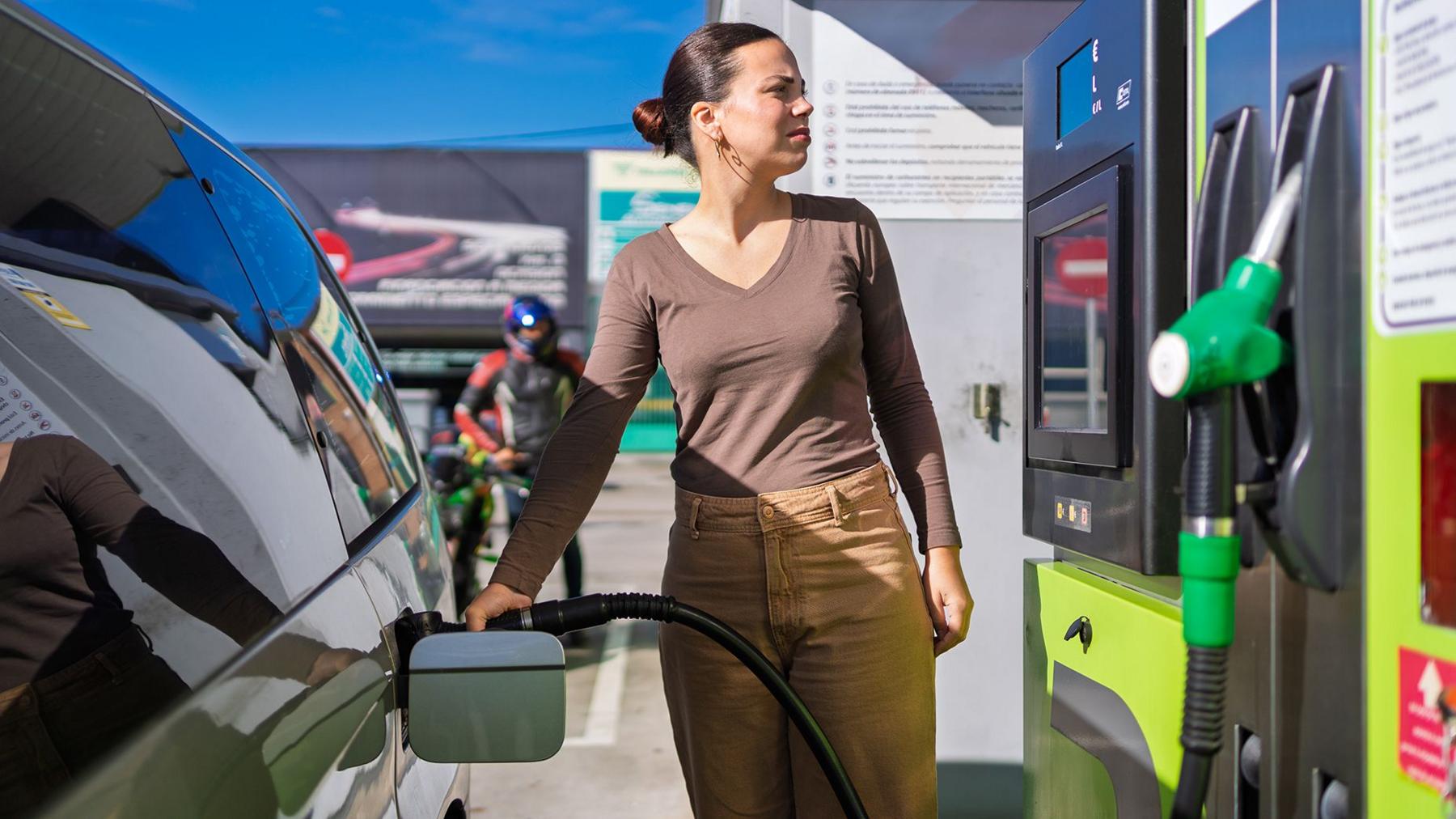 A young woman fills her car at a petrol station 