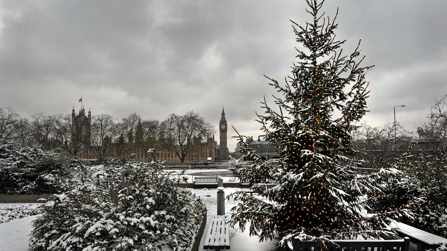 View looking over the Thames towards the houses of Parliament with a snowy scene and Christmas tree in the foreground.