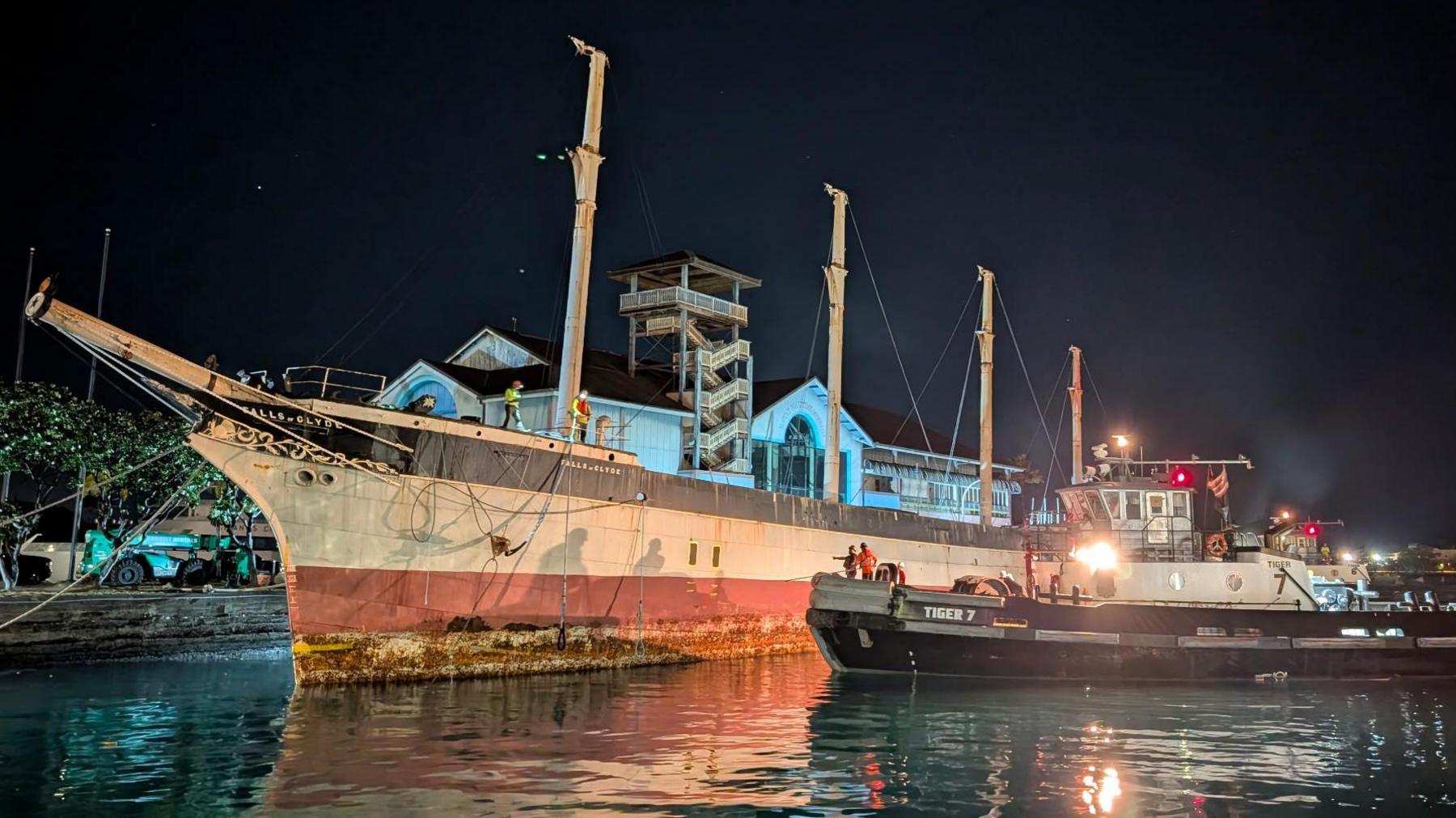 An old sailing ship with four masts with a tug beside it