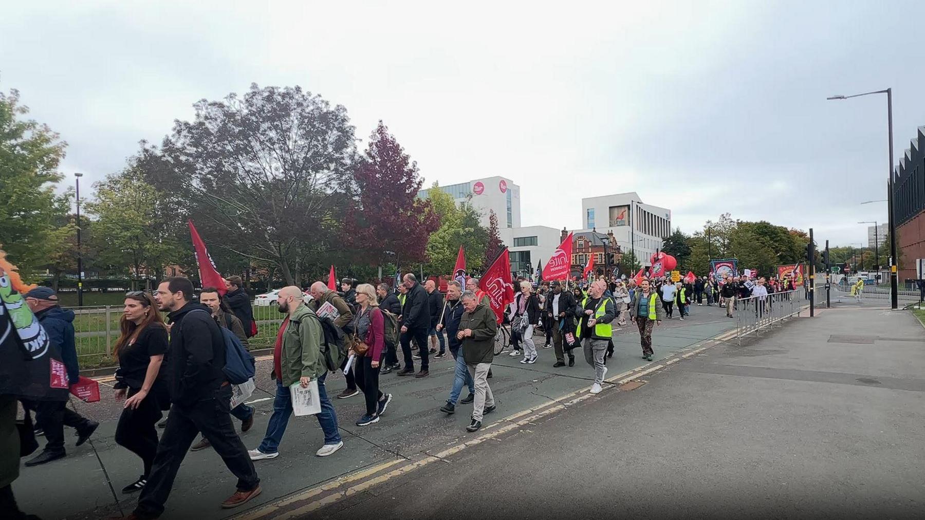 A crowd of people holding red flags walking down the street in Birmingham city centre