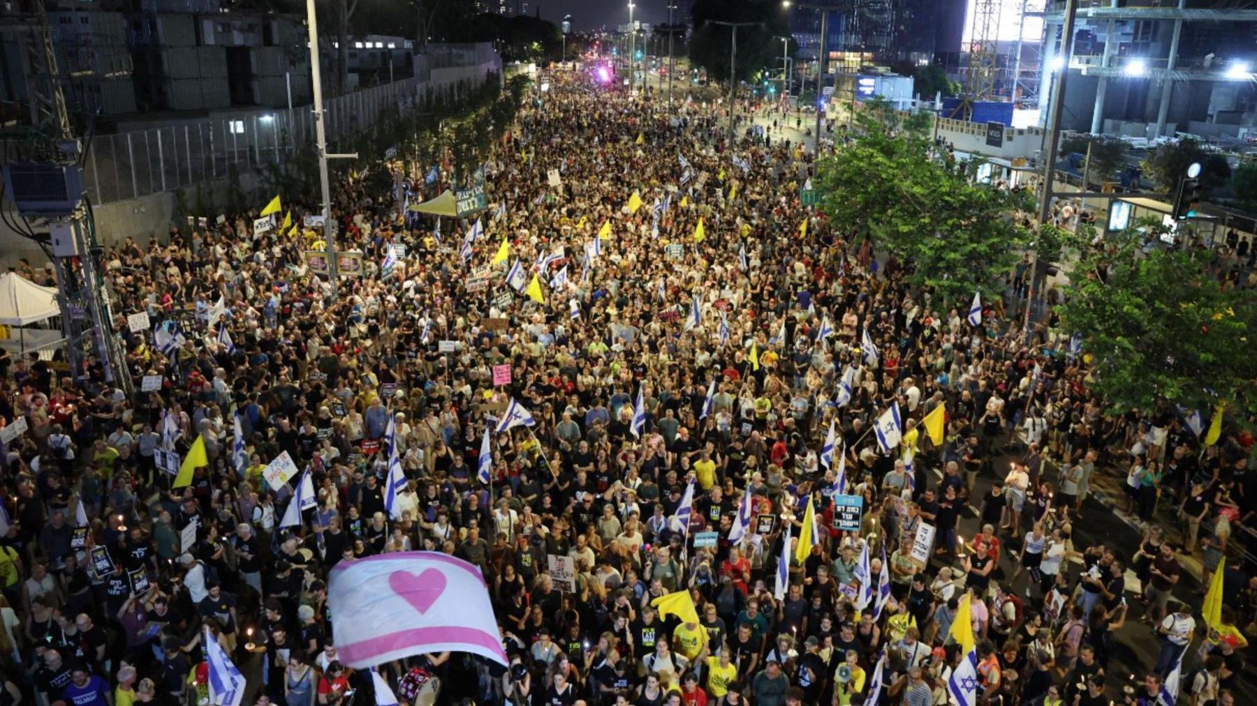 An aerial image shows a crowd of protesters filling a street, some waving yellow banners and displaying a white flag with a pink heart, calling for the release of Israeli hostages in Tel Aviv, Israel on 9 August 2025.