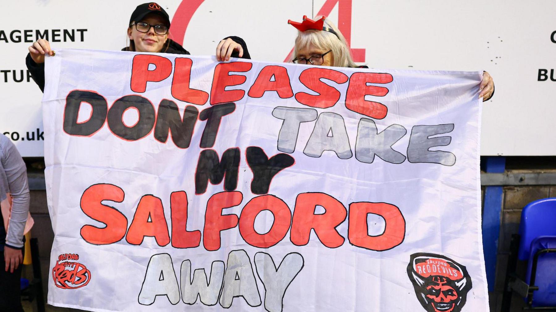 Salford Red Devils fans hold a sign which says "Don't Take My Salford Away"
