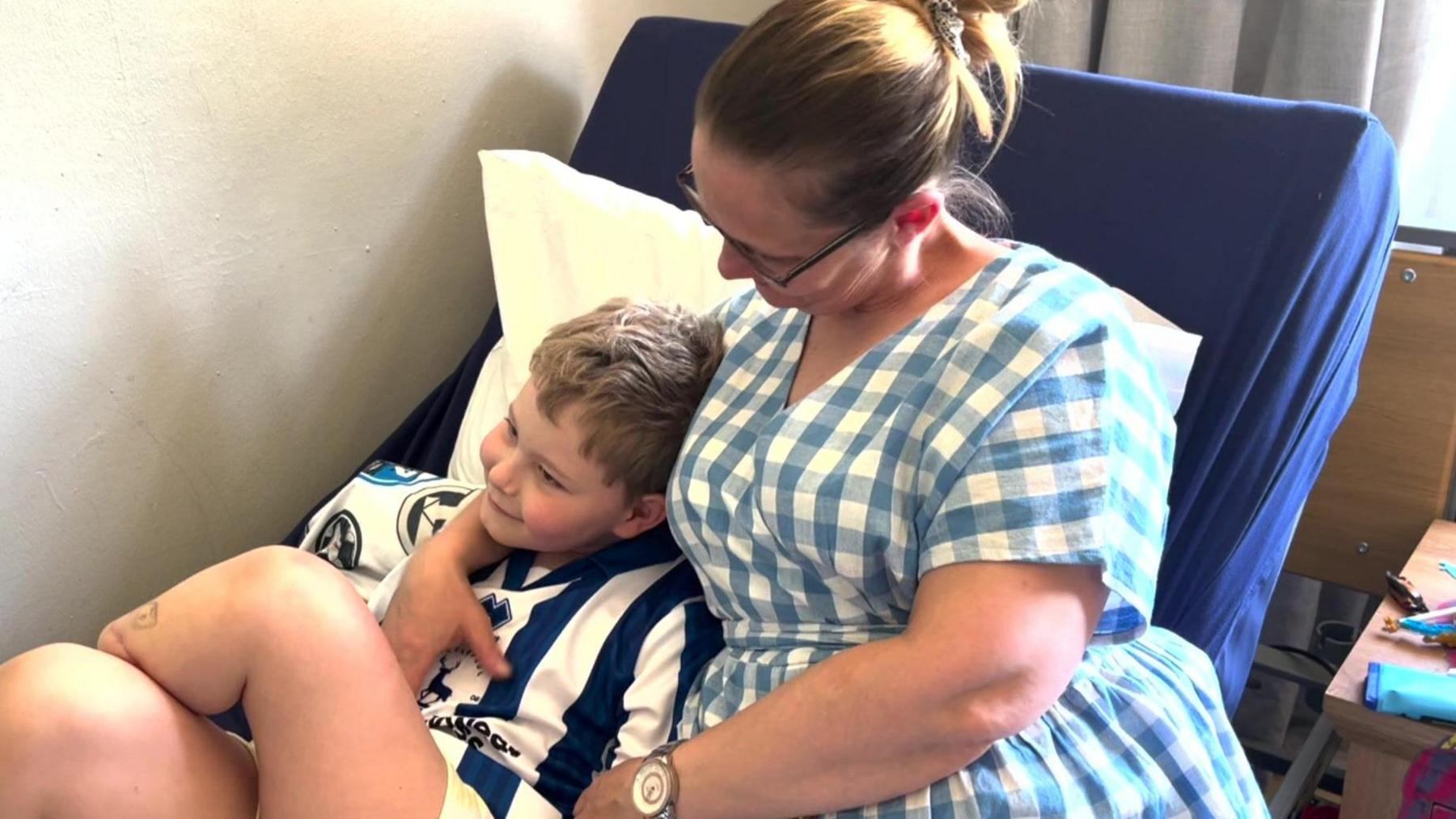 Riley Bains, aged 8, who had a lower leg amputation, lying in the arms of his mother Sarah Kidson