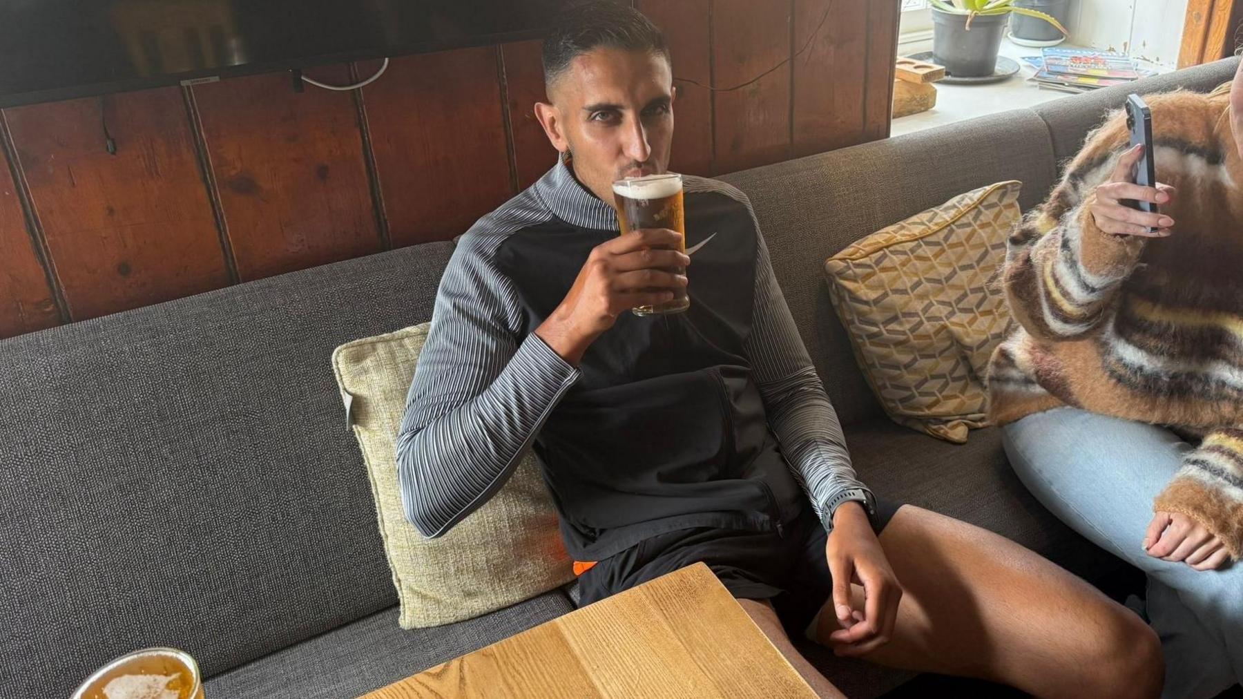 Amor Randhawa pictured at a pub in Land's End, Cornwall, after completing a 554 mile for charity. Amor is wearing a black and grey Nike top and black shorts.