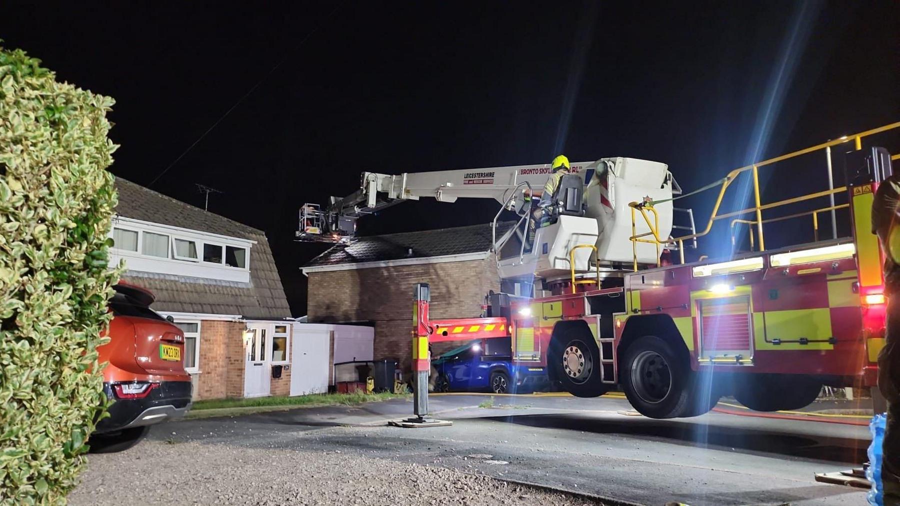 Firefighters using a hydraulic platform from a fire truck to access the roof of a house