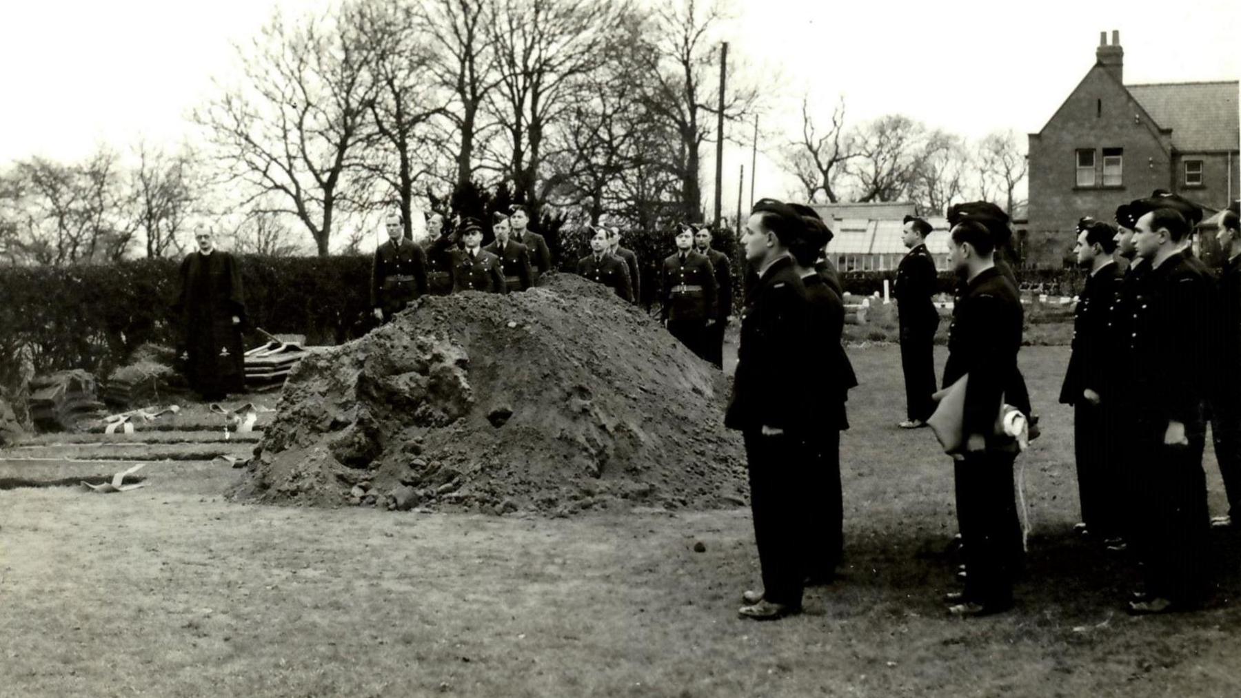 A black and white photograph of military men in uniform holding a funeral in a field.