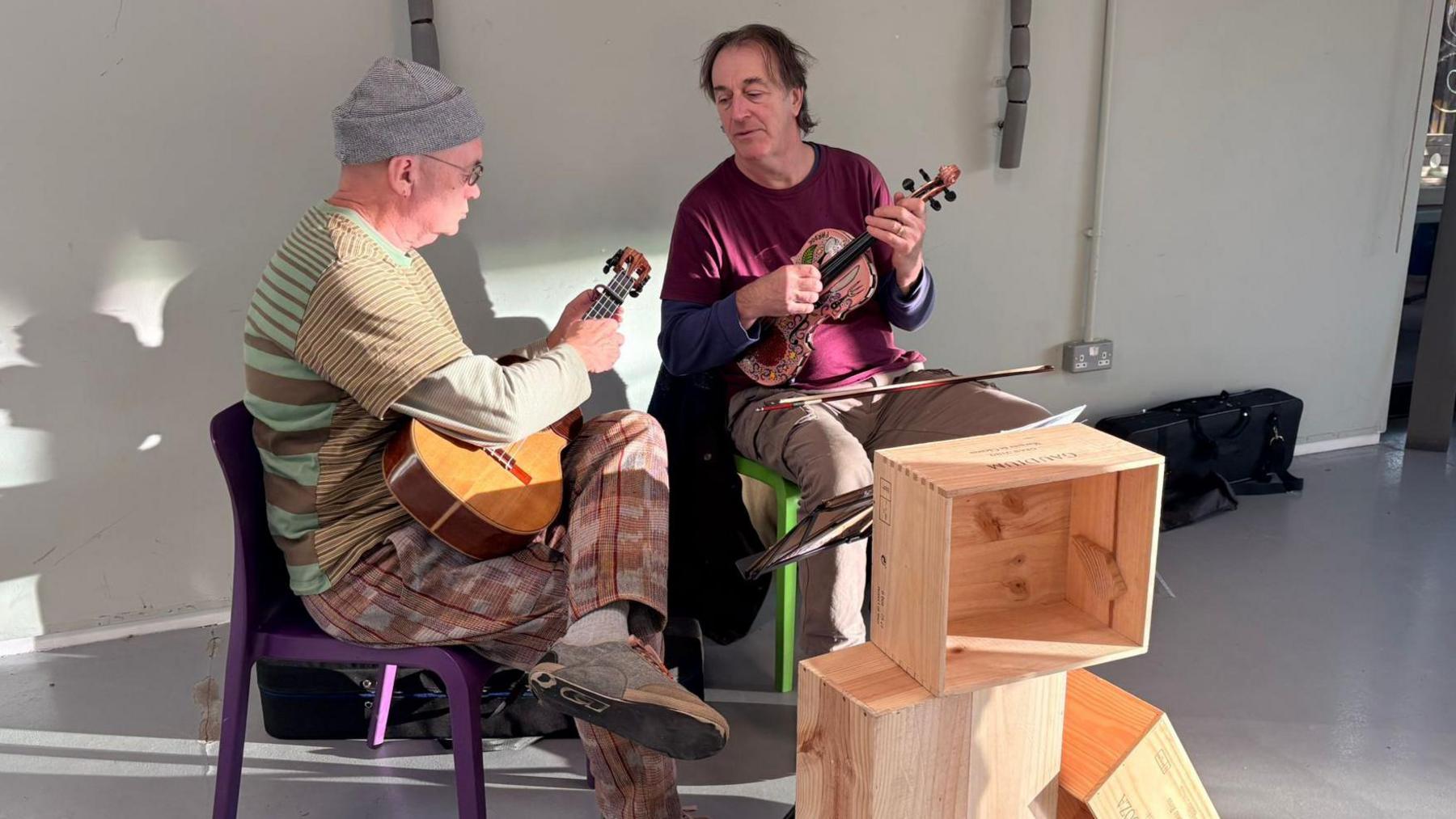 Dau ddyn yn chwarae offerynnau mewn ymarferion. Mae bocsys pren o'u blaenau.