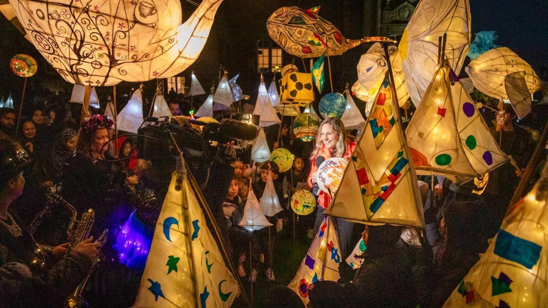 A lantern parade with people and children smiling and carrying multi-coloured paper lanterns with lights inside