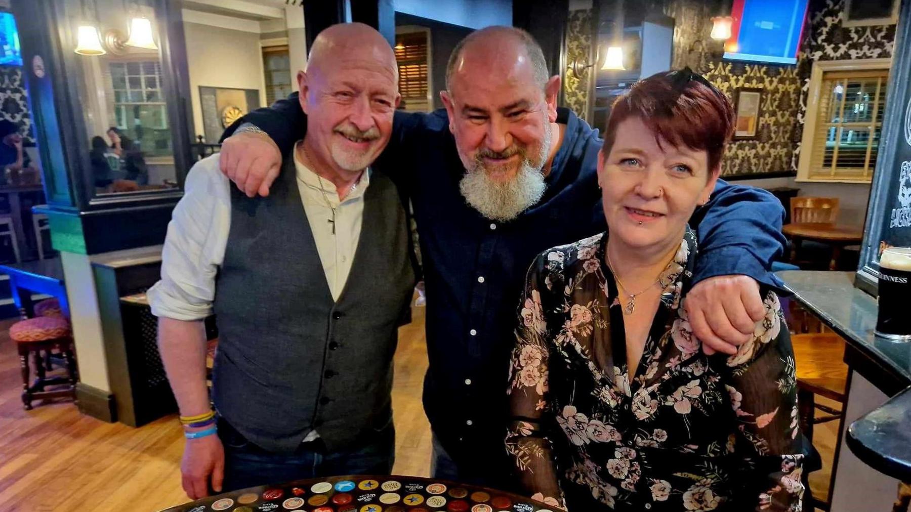 Andrew Reilly, John Rawcliffe and Maddy Howard hugging in a pub at one of the meetings