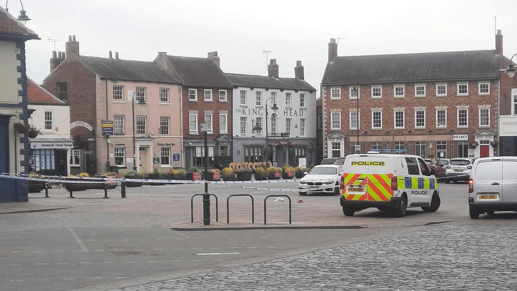 A police cordon on Beverley's Saturday Market. There are police vehicles and discarded clothes on the ground